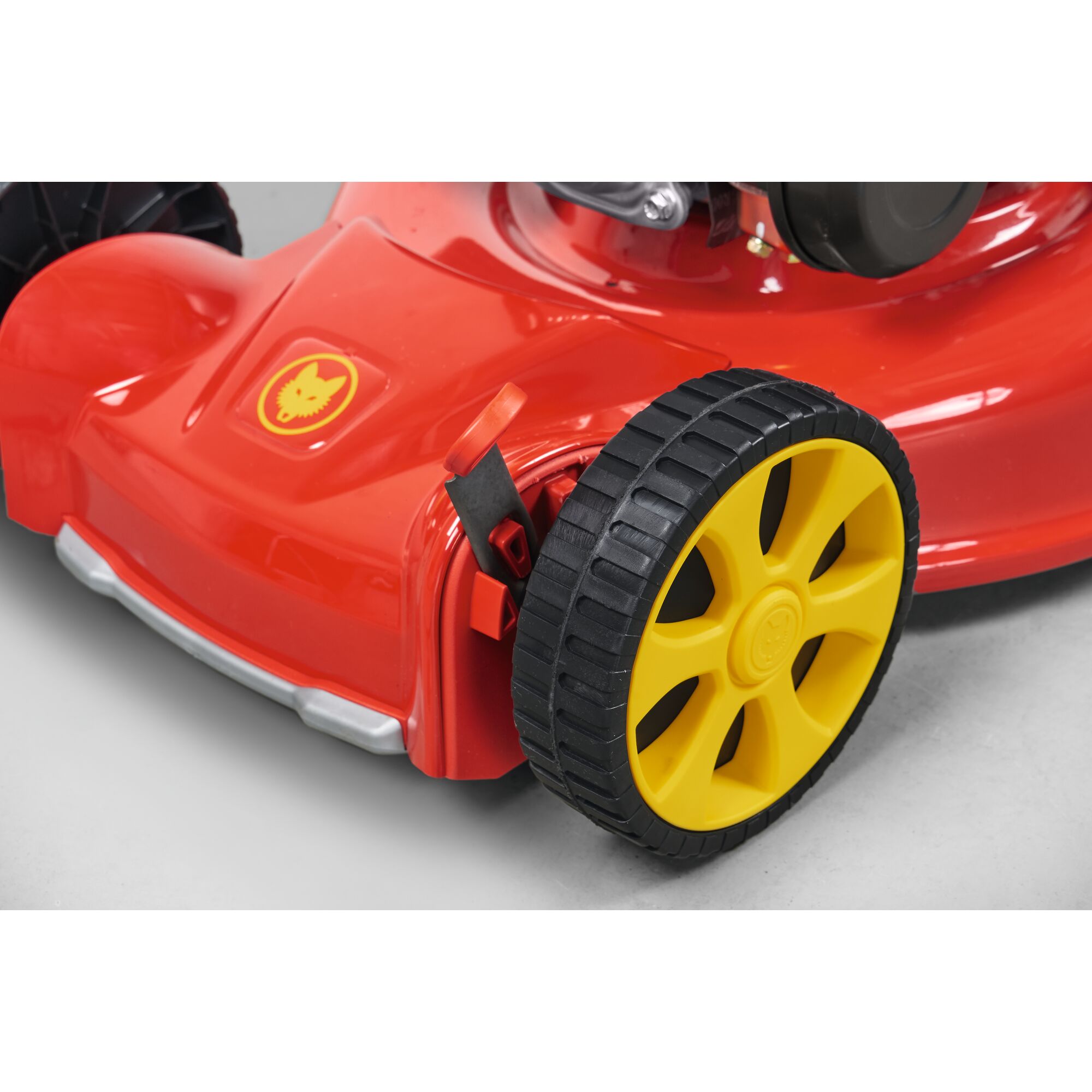 Close-up of a red lawn mower showing a yellow wheel and adjustment lever on the side. The lawn mower features the WOLFGarten logo on the body.