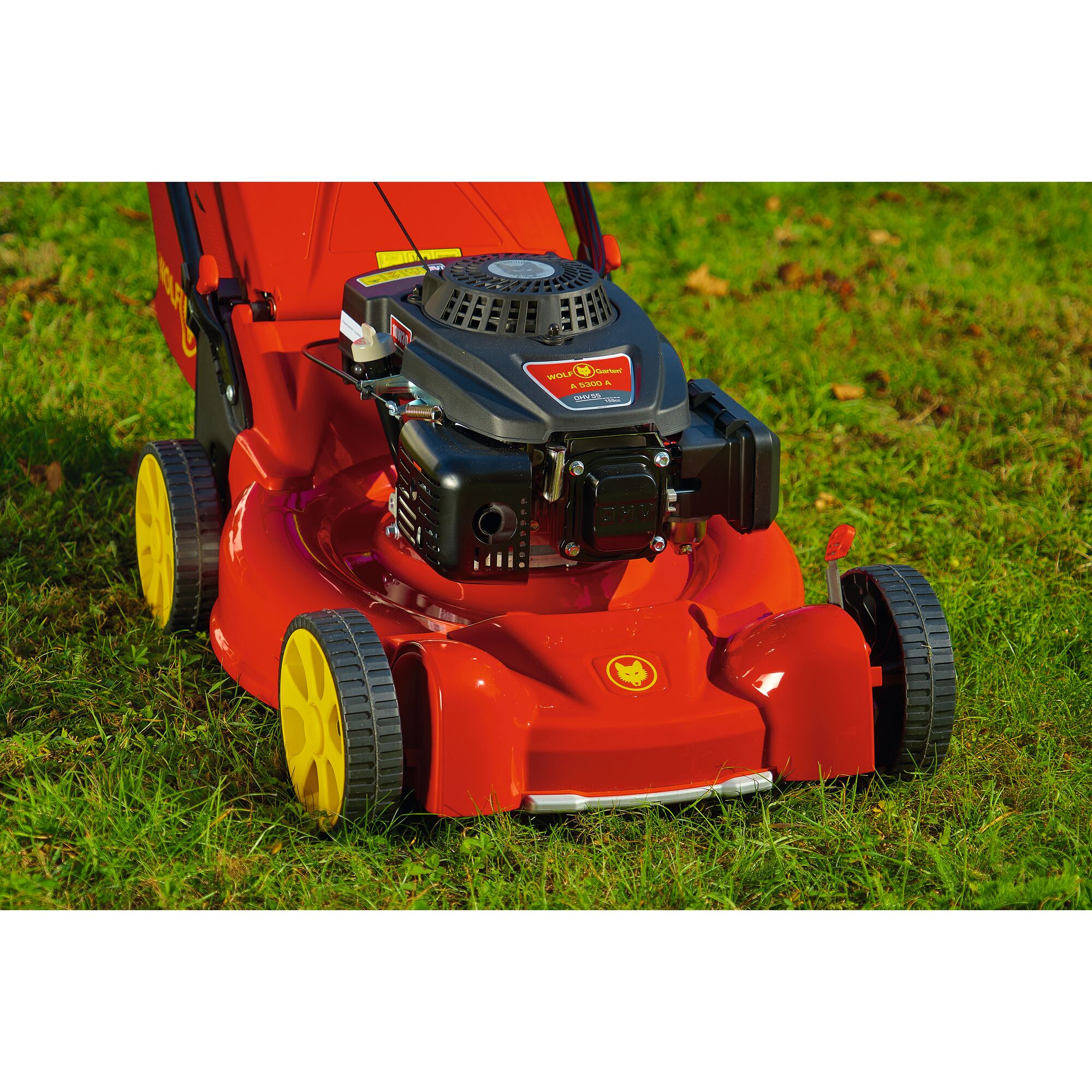 Close-up image of a red and black WOLF-Garten lawn mower with yellow wheels, placed on grass outdoors.