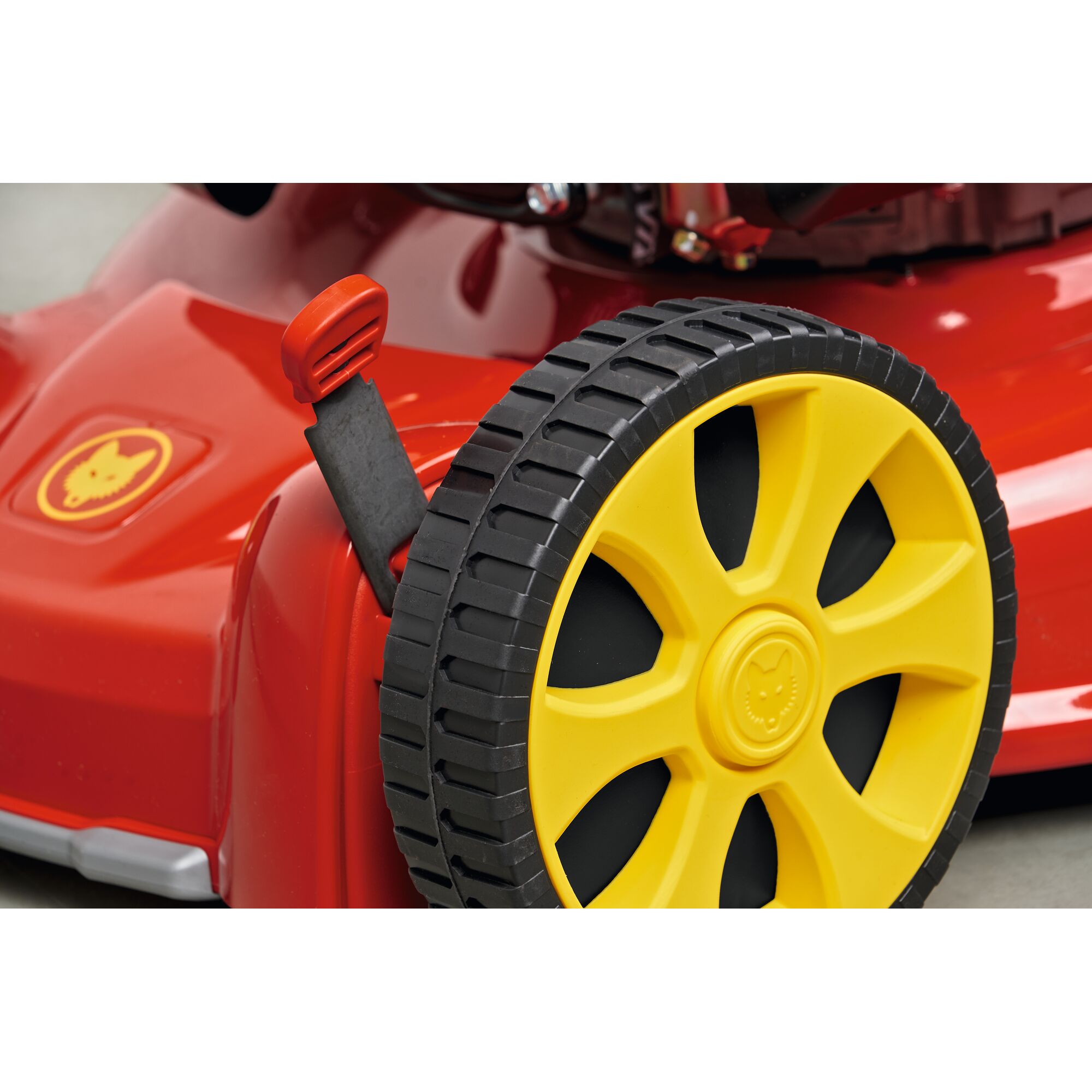 Close-up of the wheel and height adjustment lever of a red and yellow WOLFGarten lawn mower.