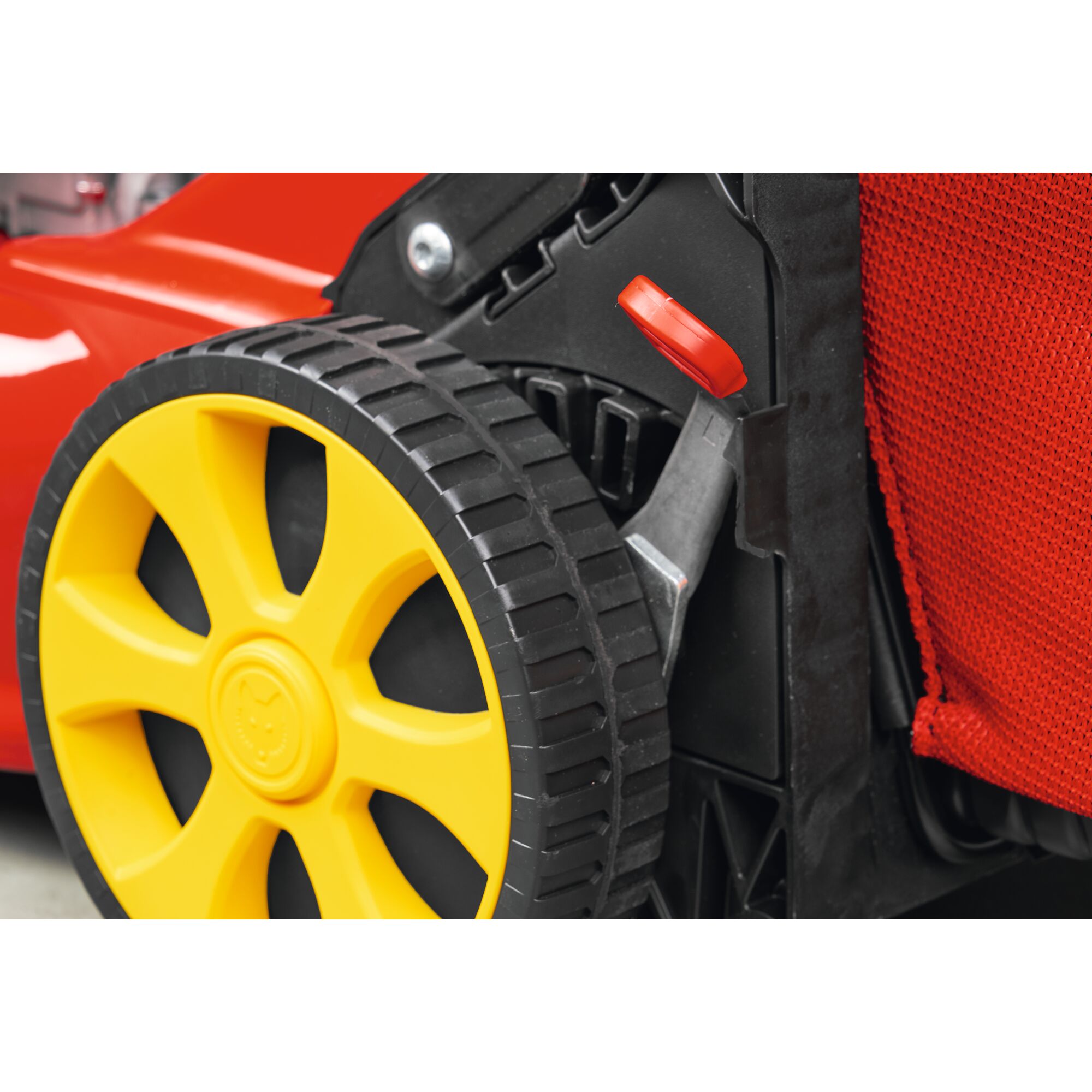 Close-up of a yellow wheel with a black tire on a red and black garden tool, featuring a red lever and a textured red fabric bag.