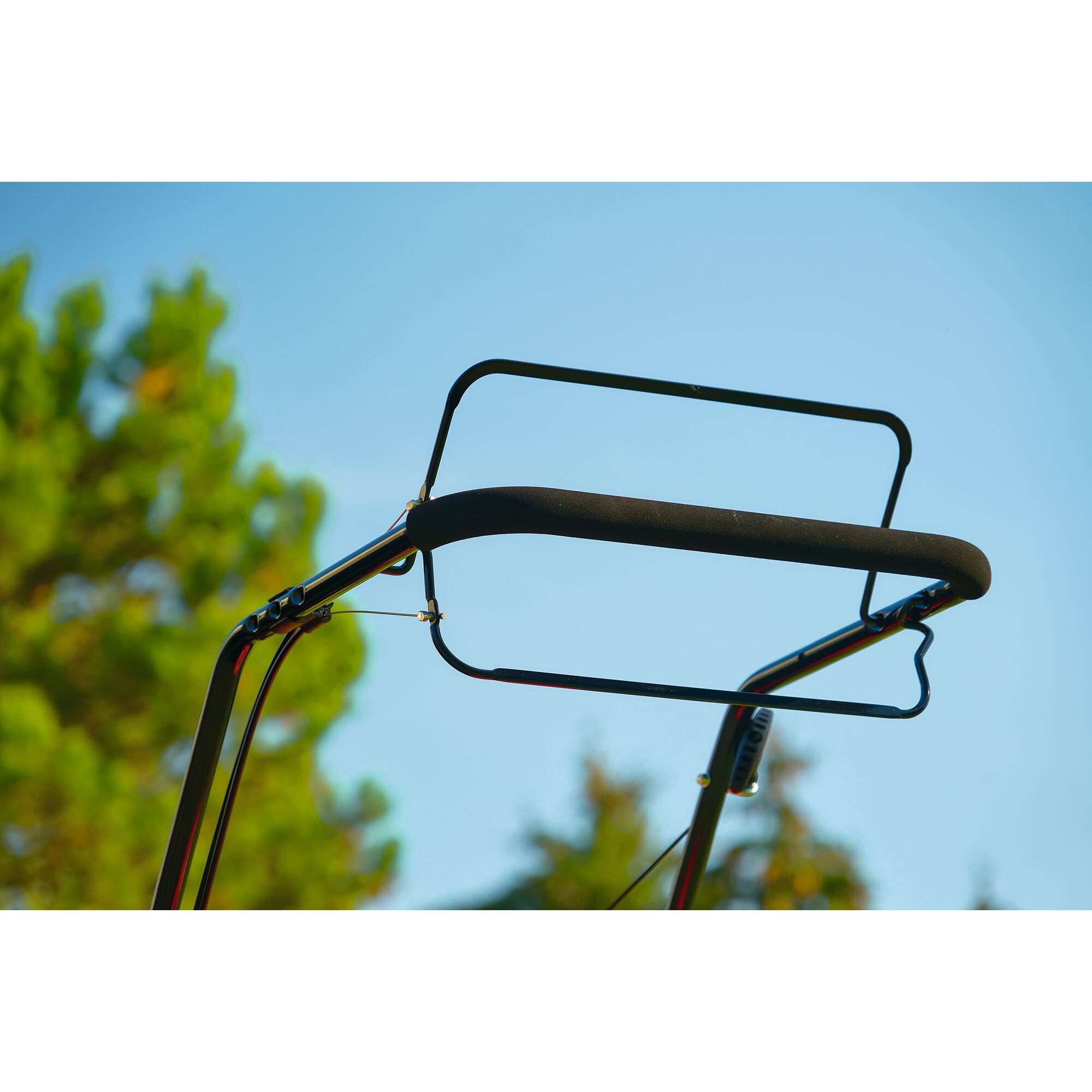 Close-up of the handlebar of a garden lawn mower, with a soft grip and metal frame, photographed outdoors against a blue sky.