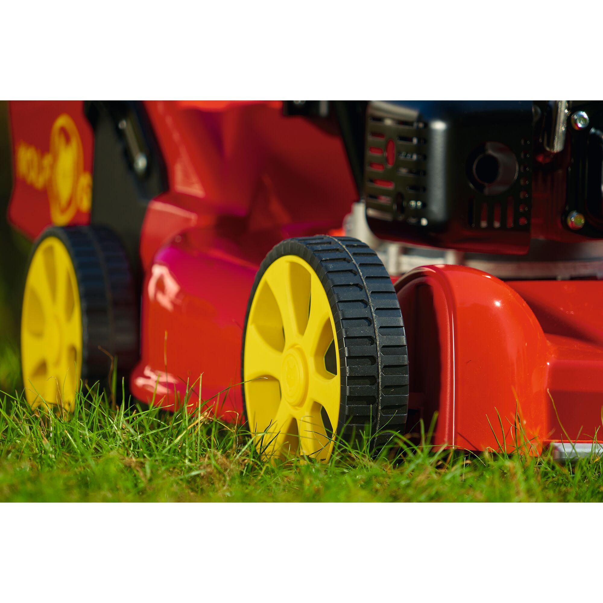 Close-up view of a red lawn mower with yellow wheels on grass.