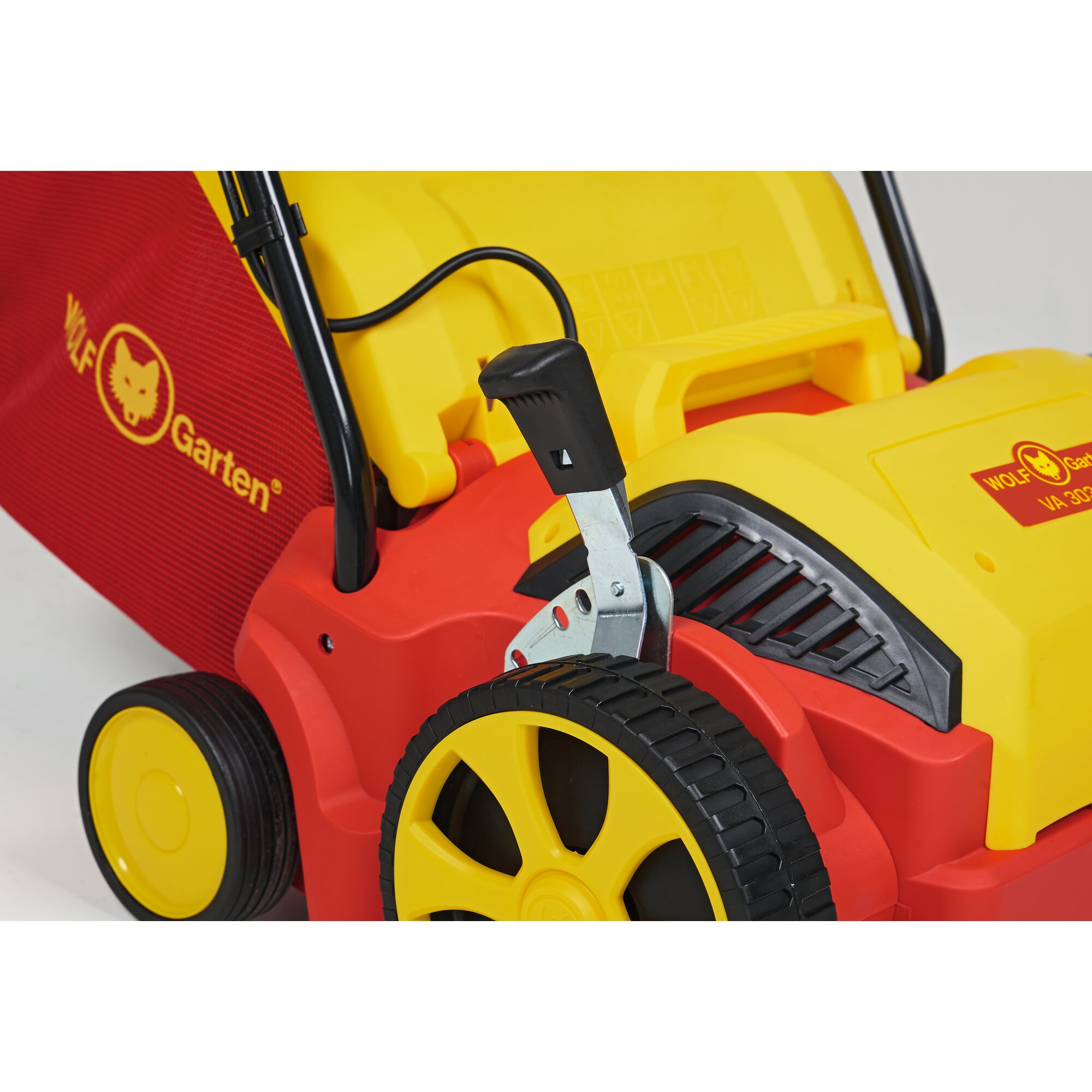 Close-up of a WOLF Garten lawn mower, featuring bright red and yellow coloring, a black handle, a yellow wheel, and the brand logo on the side.