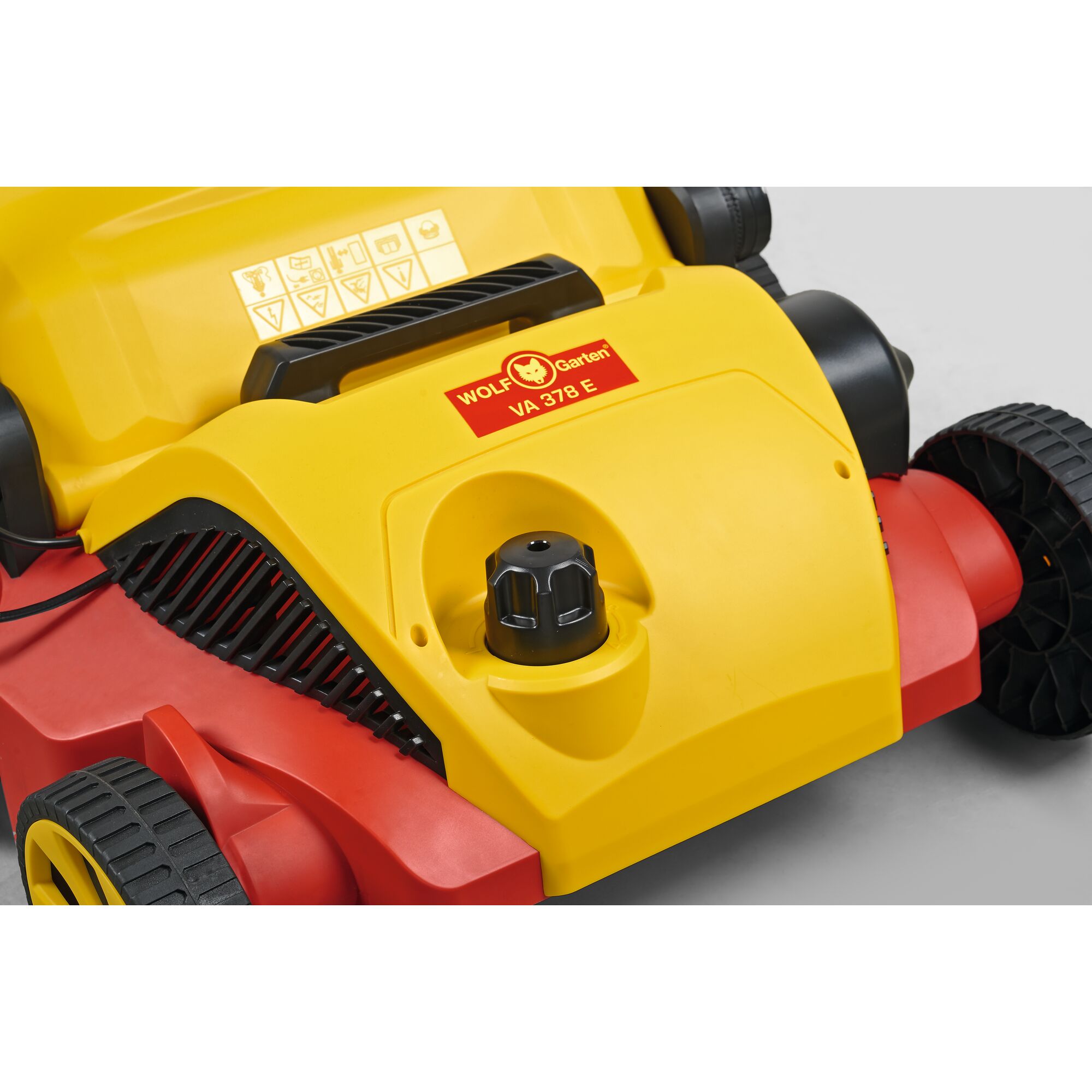 Close-up image of a WOLF Garten lawn scarifier model VA 378 E, showing part of the yellow and red body, adjustment knob, wheels, and control handle.