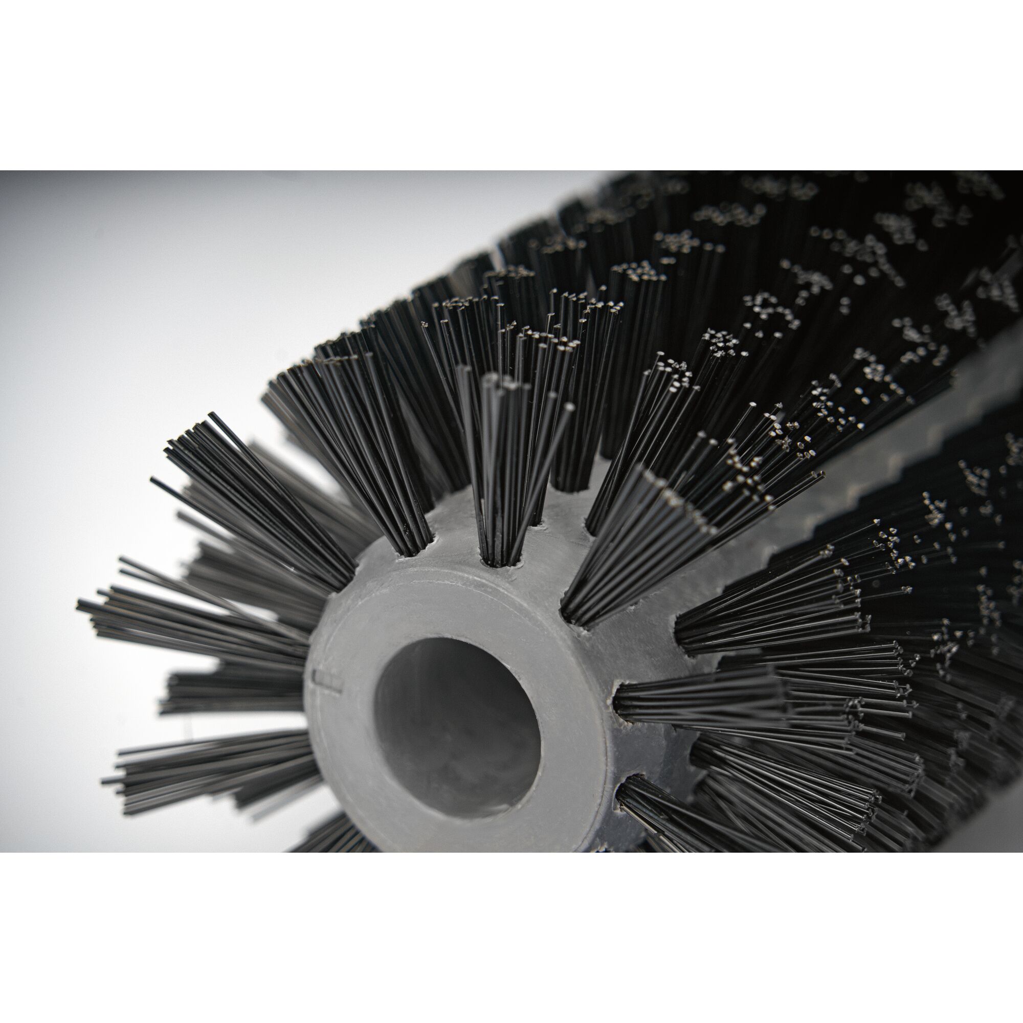 Close-up of a cylindrical brush with dense black bristles and a central hollow core, typically used for cleaning or sweeping.
