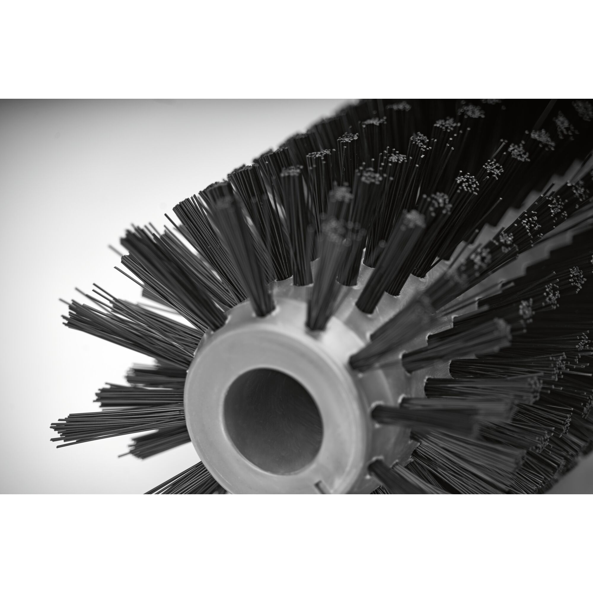 Close-up view of a cylindrical brush with dense, stiff bristles arranged in circular rows around a central core. The brush is likely used as an attachment for cleaning or sweeping equipment.
