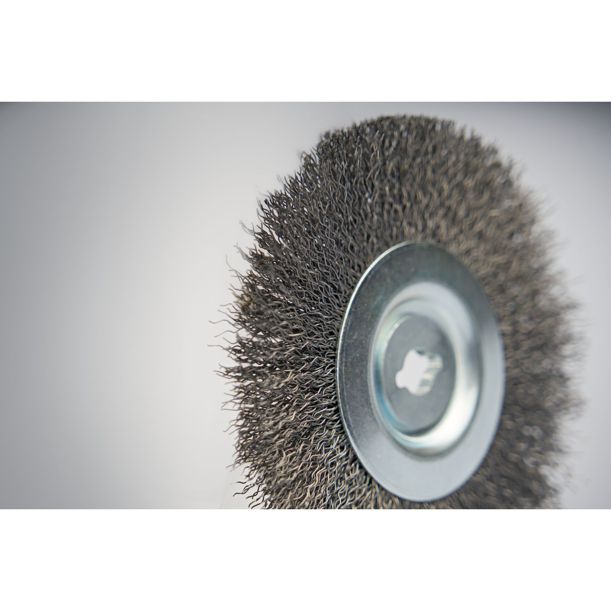 Close-up image of a round wire brush with metal bristles and a central metal hub, typically used for cleaning, removing rust, or surface preparation.