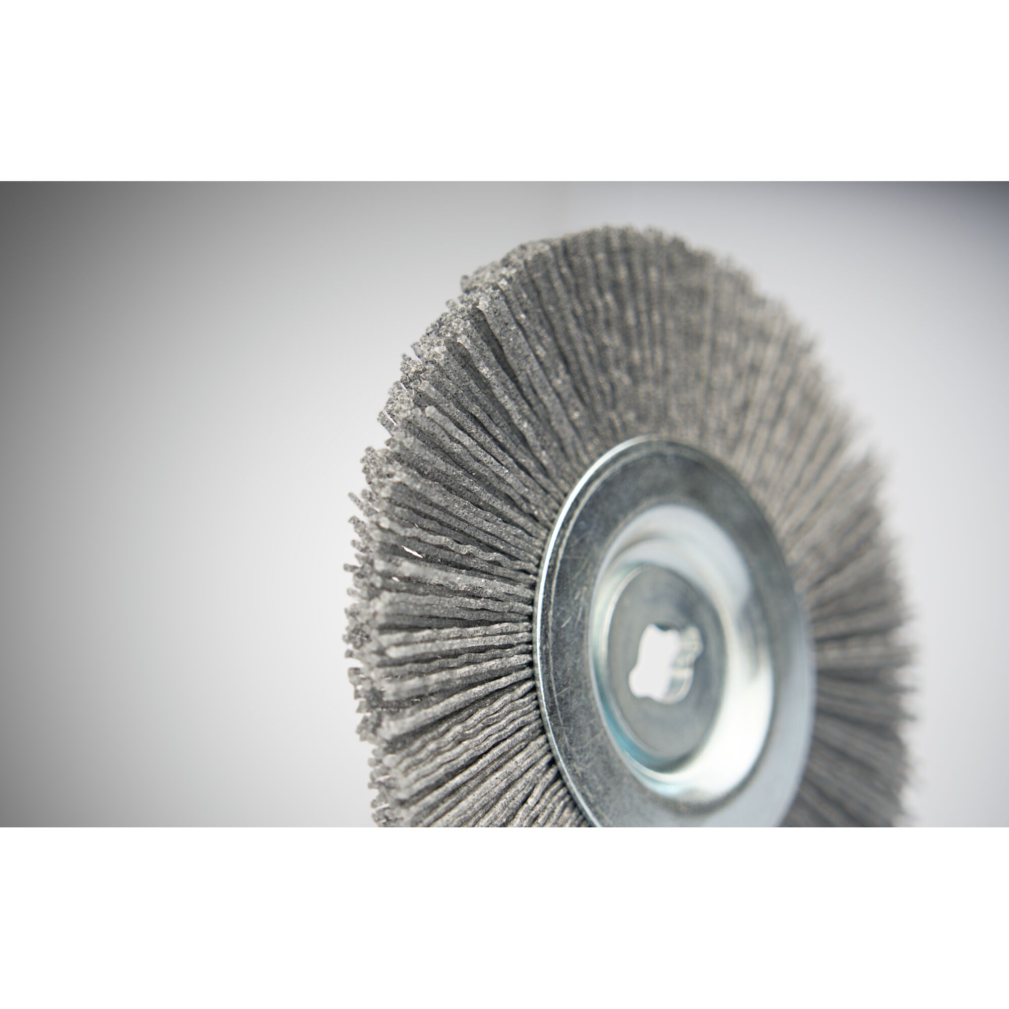 Close-up of a circular wire brush, featuring stiff bristles and a metal center, used for cleaning or polishing surfaces.