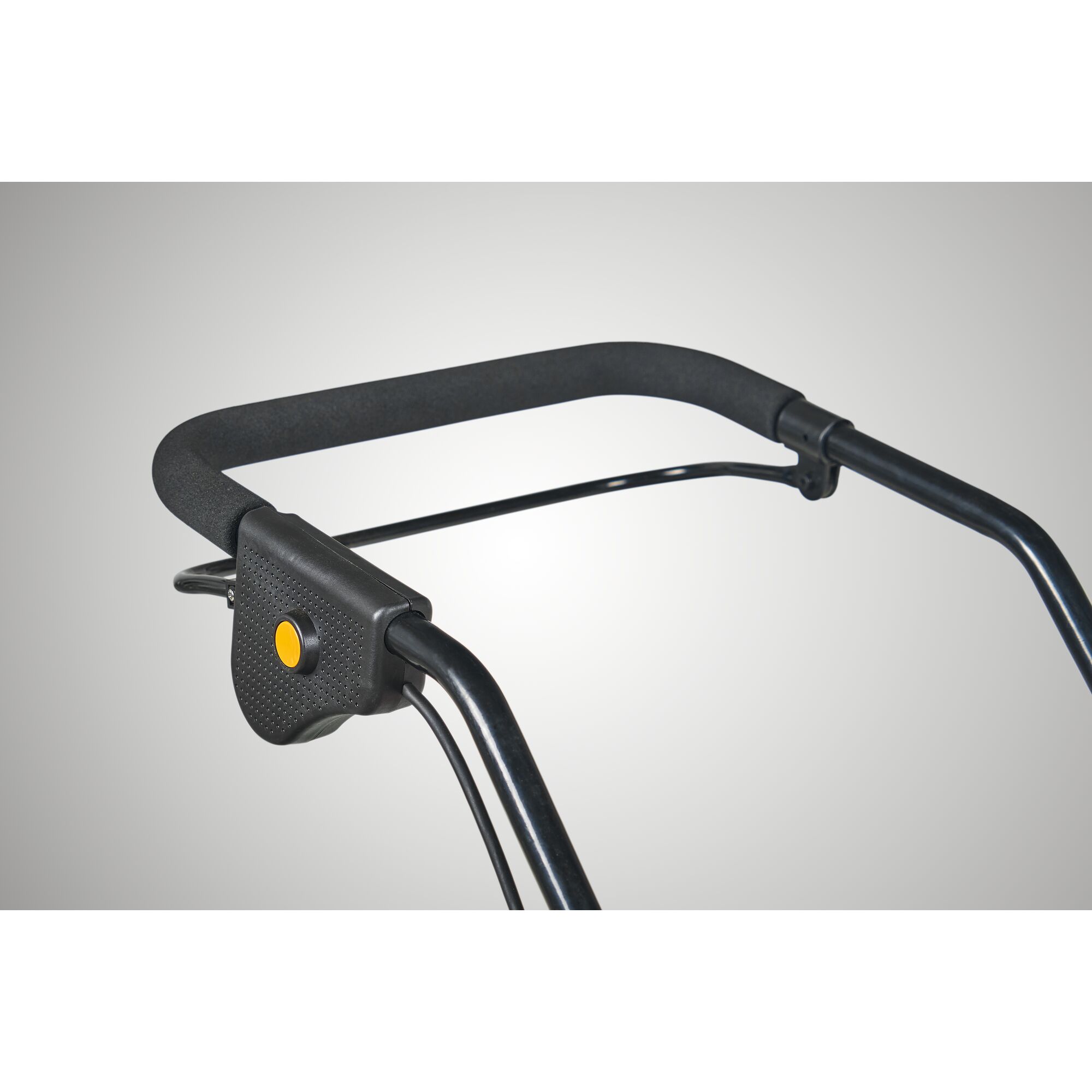 Close-up view of a black handlebar with a foam grip and a yellow-button control, likely part of a garden tool or lawn mower.