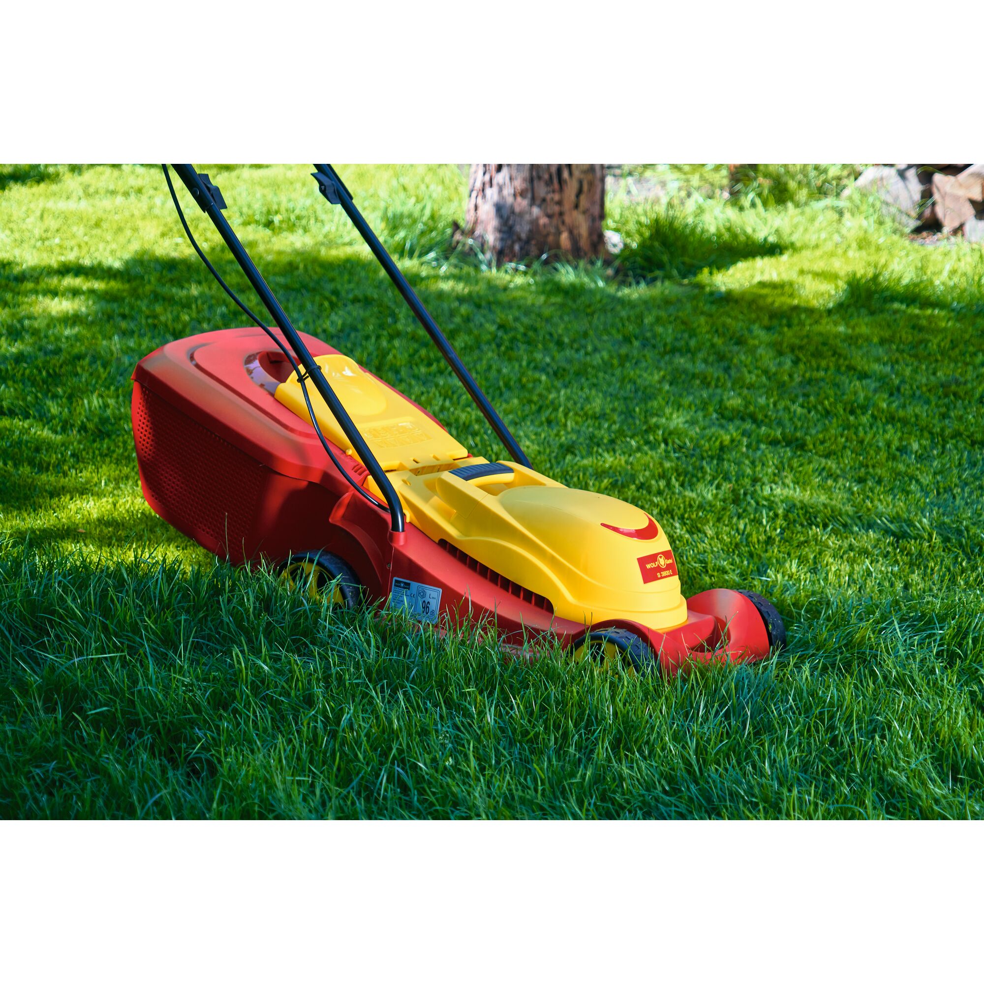 A yellow and red WOLFGarten lawn mower is pictured cutting grass outdoors.