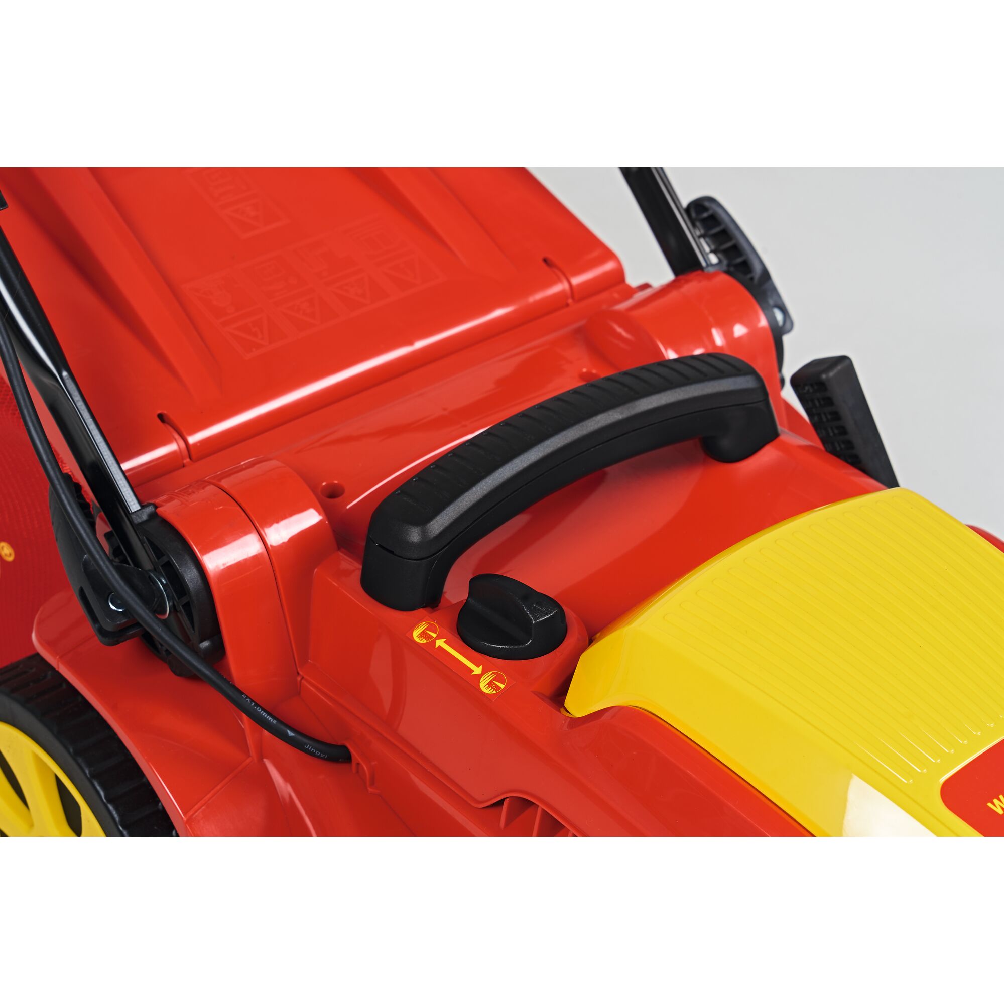 Close-up of the control handle and adjustment knob on a WOLFGarten lawn mower, showing red and yellow plastic parts and details of the mechanism.