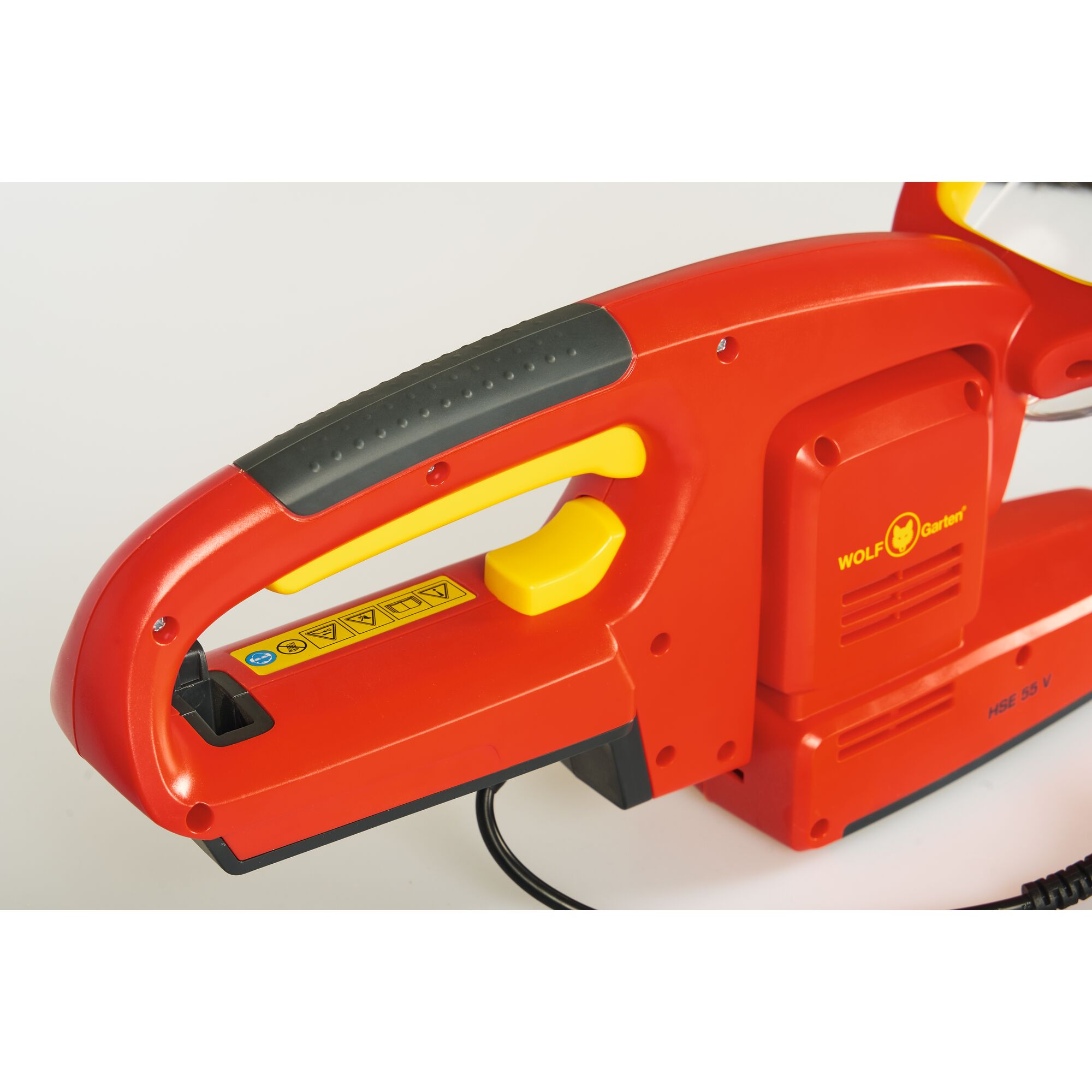 Close-up view of the handle and controls of a red and yellow WOLF-Garten electric hedge trimmer, showing the trigger and safety symbols.