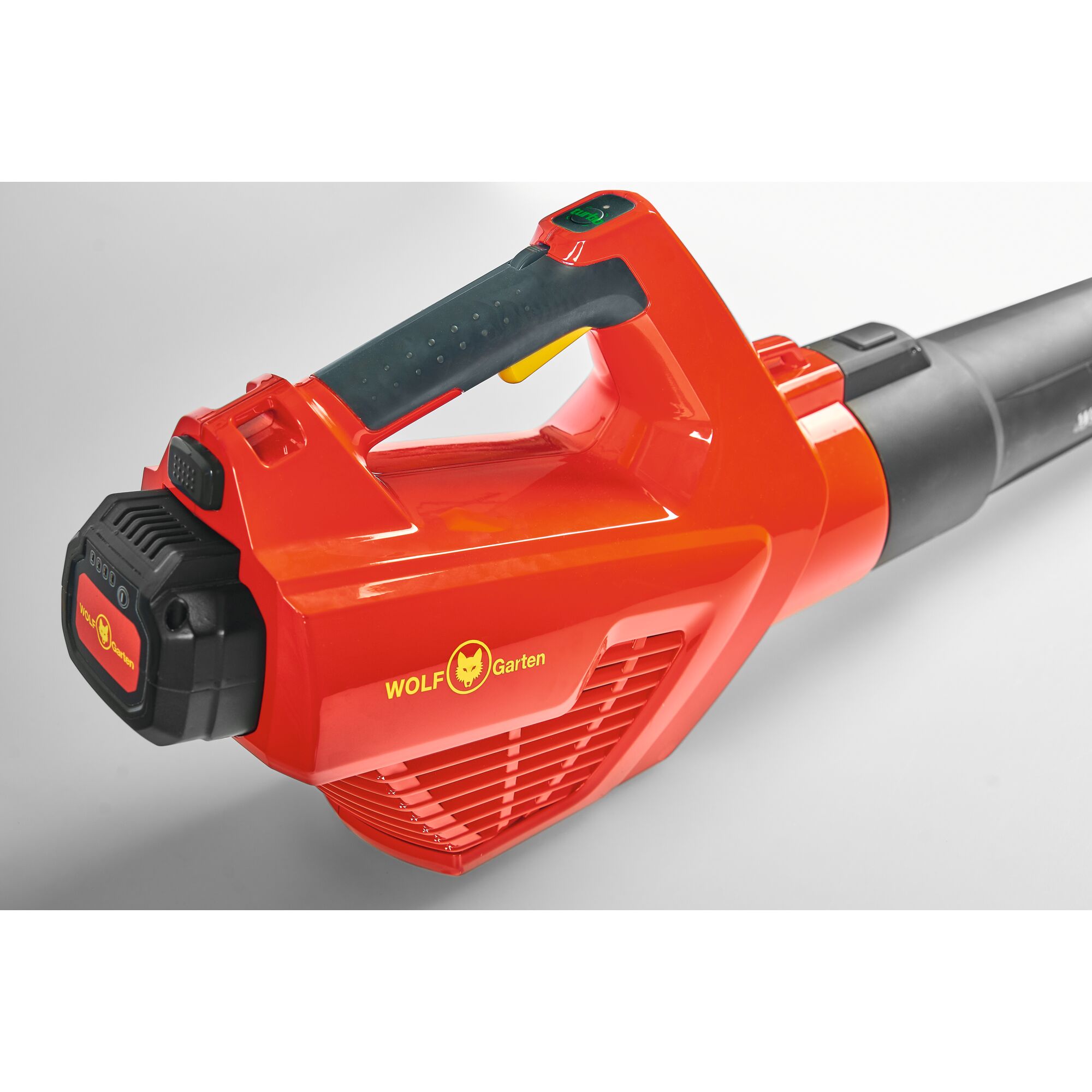 A close-up view of a red and black WOLF Garten battery-powered leaf blower, showing its handle, battery pack, and air intake grille.