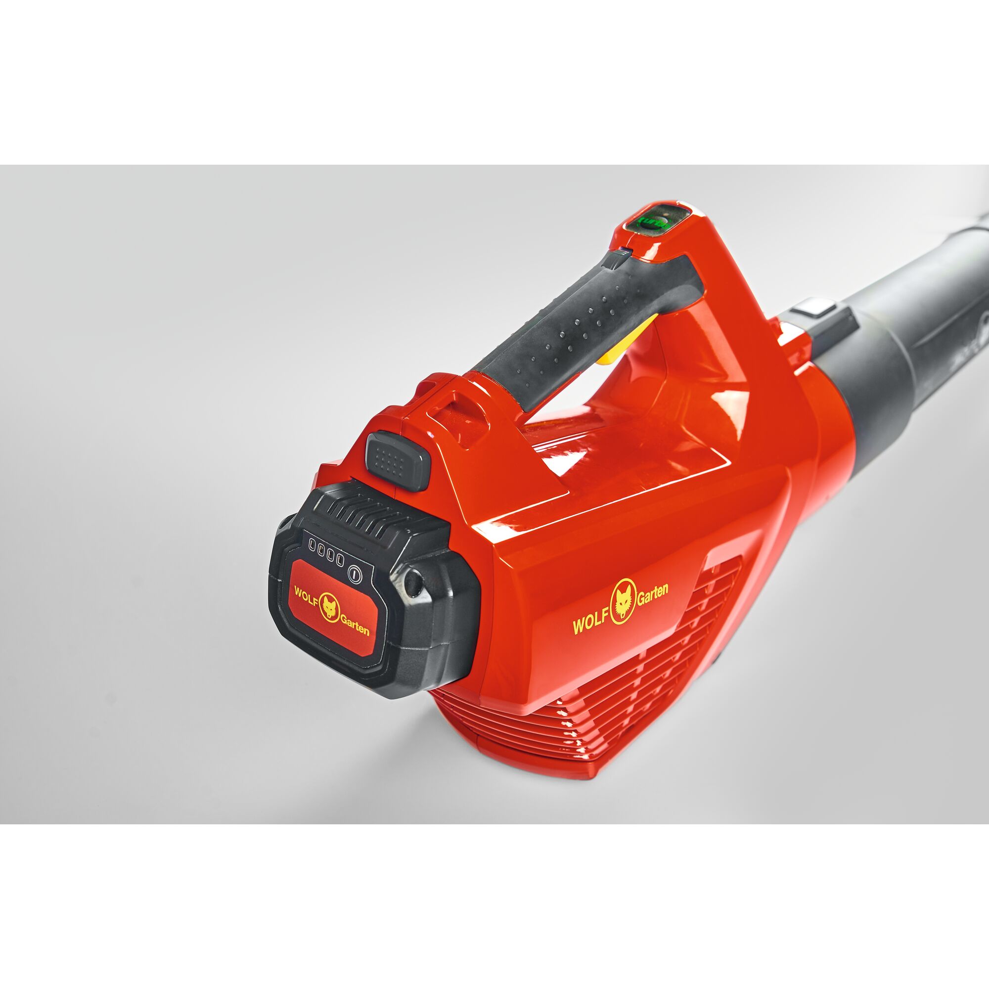 Close-up view of a WOLF Garten red leaf blower with a black handle and battery pack attached, featuring the WOLF Garten logo on the side.