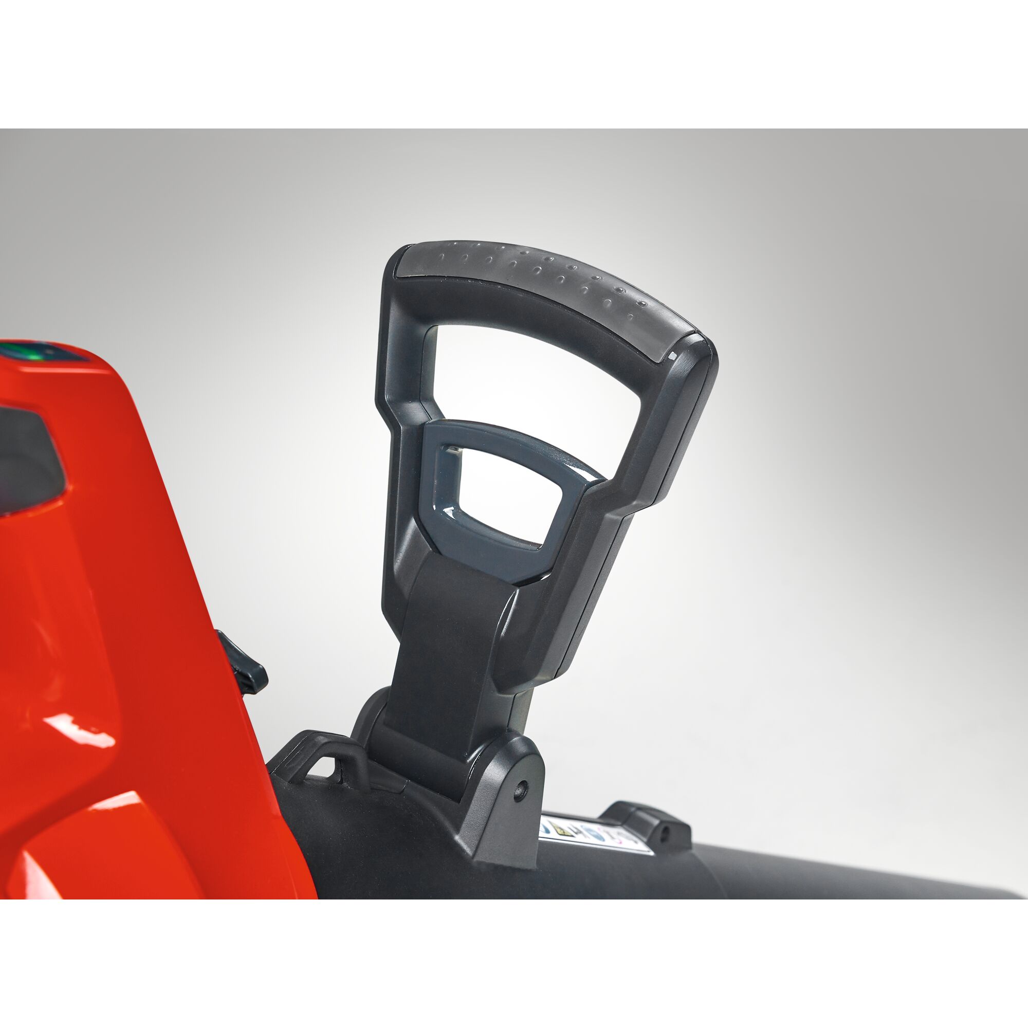 Close-up of a black ergonomic handle attached to a red and black machine, photographed against a neutral background.