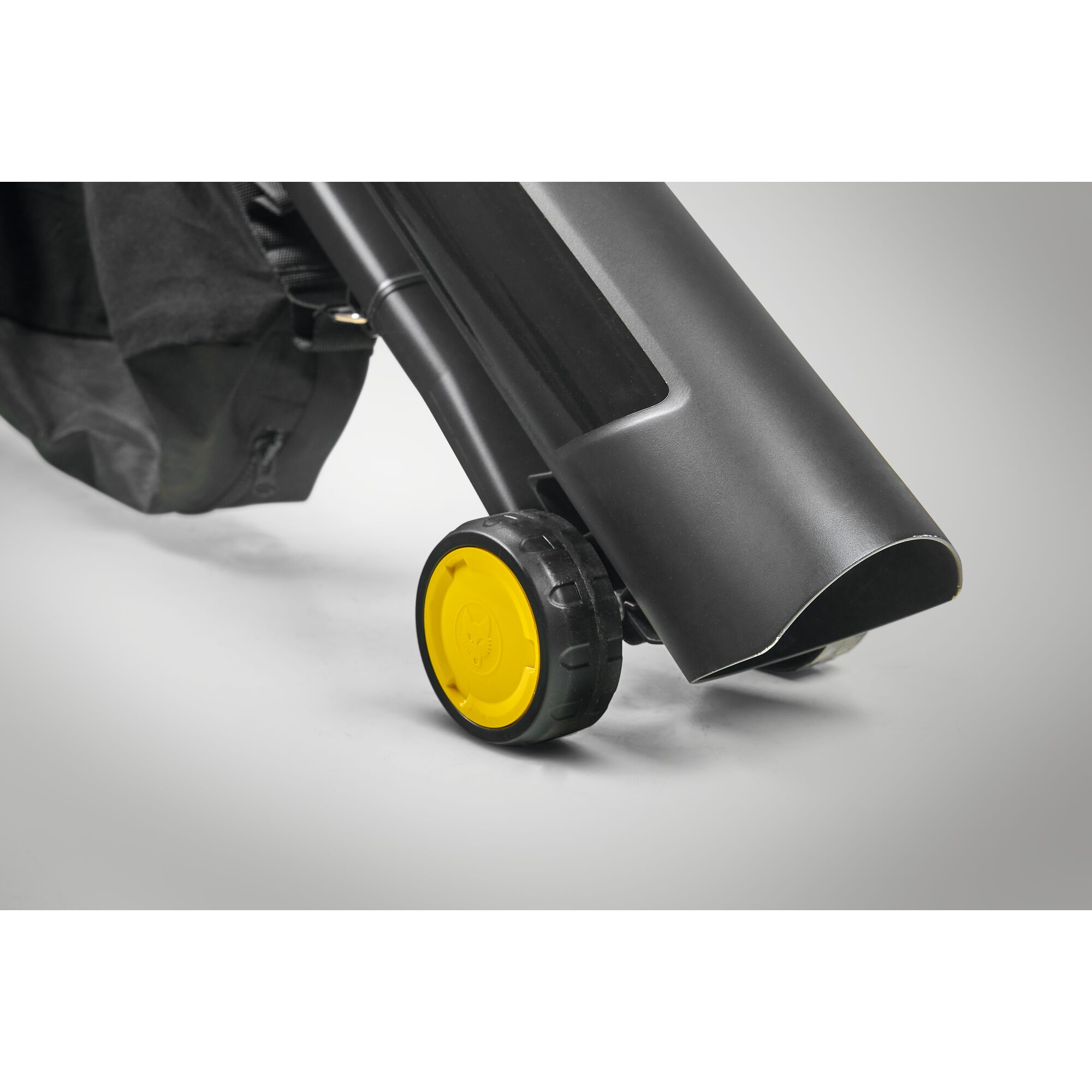 Close-up view of a gardening tool with a black wheel featuring a yellow center, attached to a black plastic tube and a fabric bag.