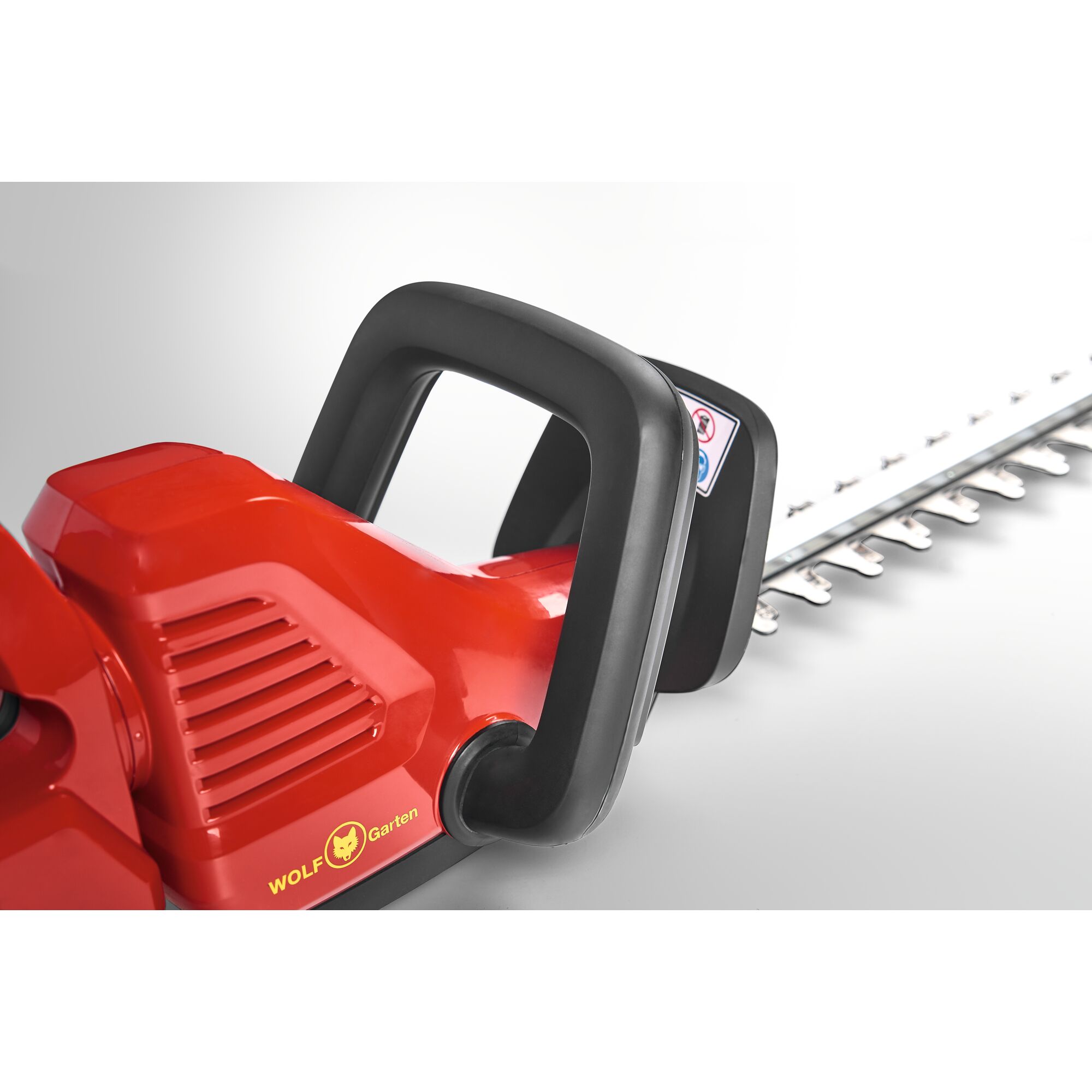 Close-up of a WOLF-Garten electric hedge trimmer showing the red body, black handle, and part of the cutting blade.