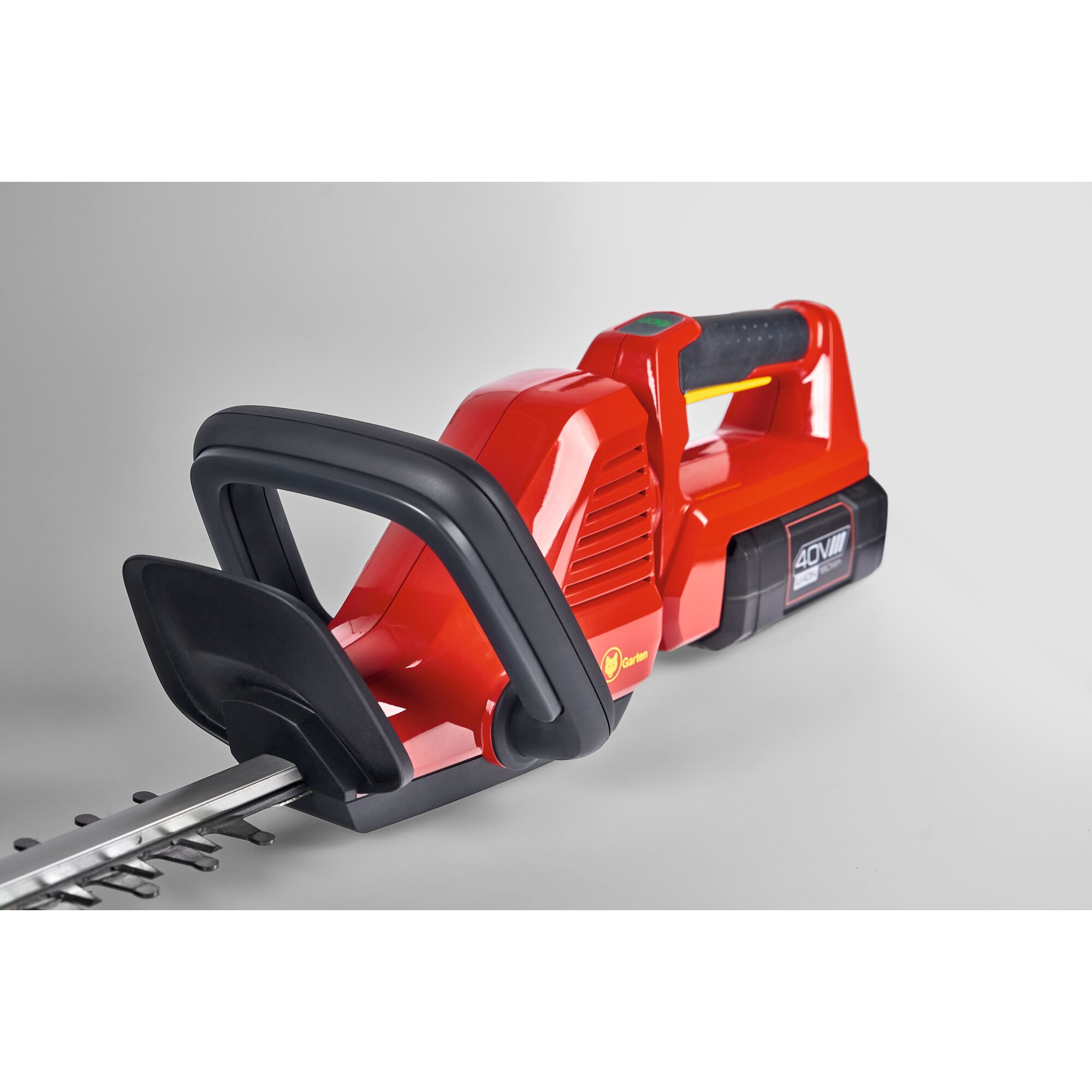 A close-up view of a red and black cordless hedge trimmer with a visible battery pack, featuring a front handle and part of the cutting blade.