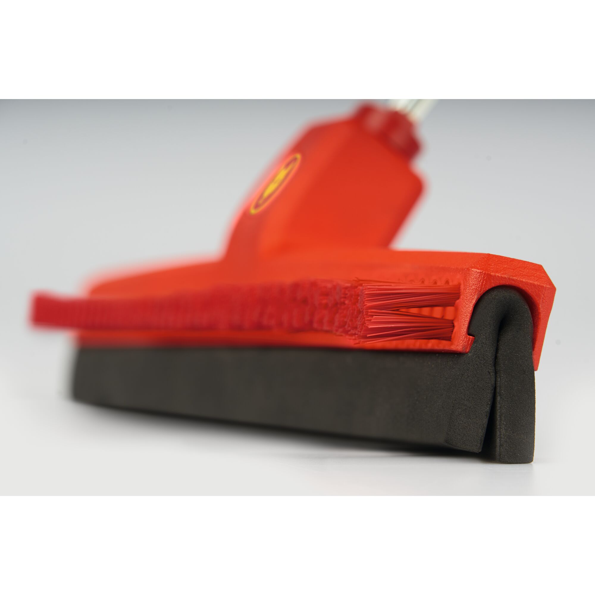 Close-up of a red cleaning broom head with firm bristles and a black rubber squeegee attached underneath, designed for efficient sweeping and water removal.