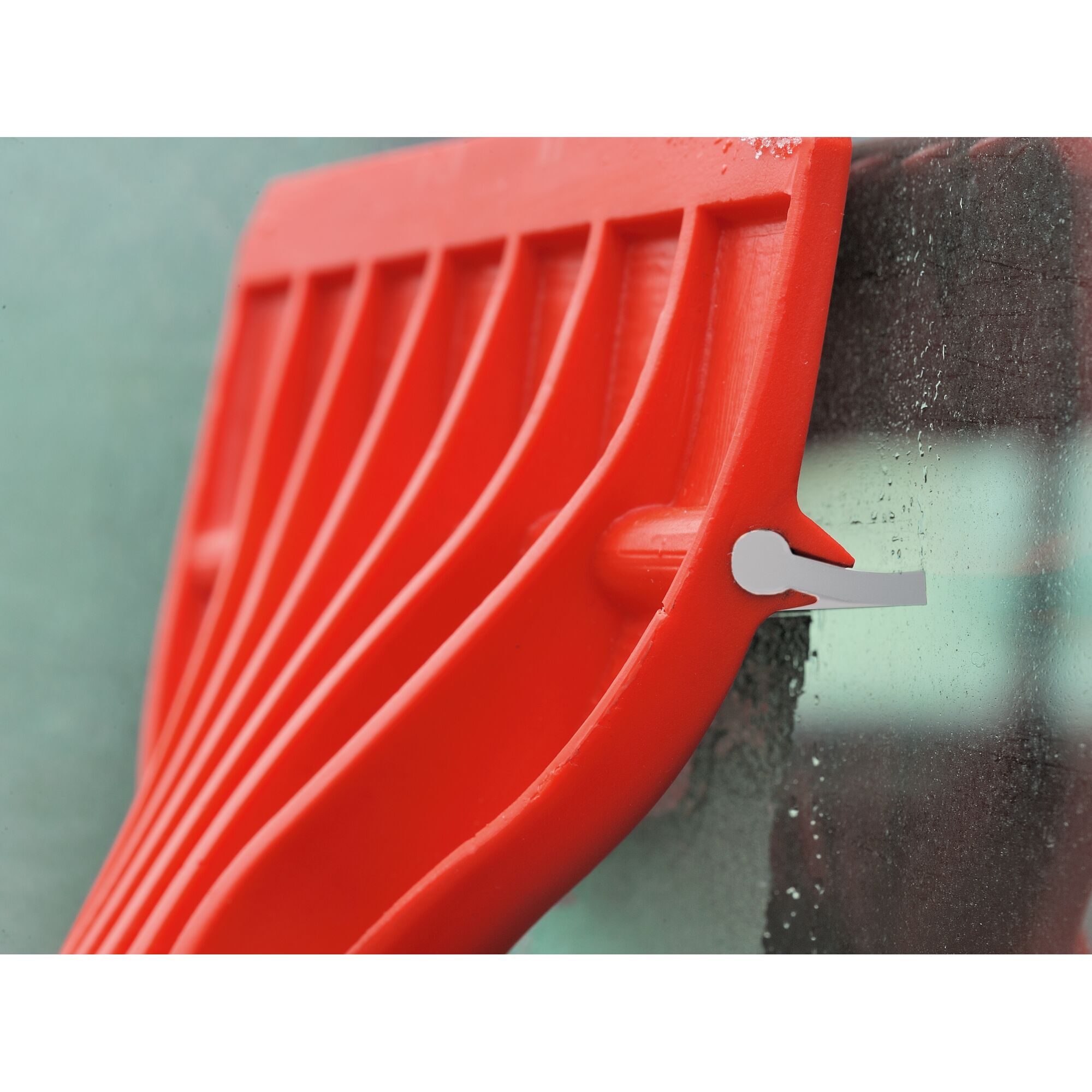 Close-up of a red plastic ice scraper being used to clean a frosted window.