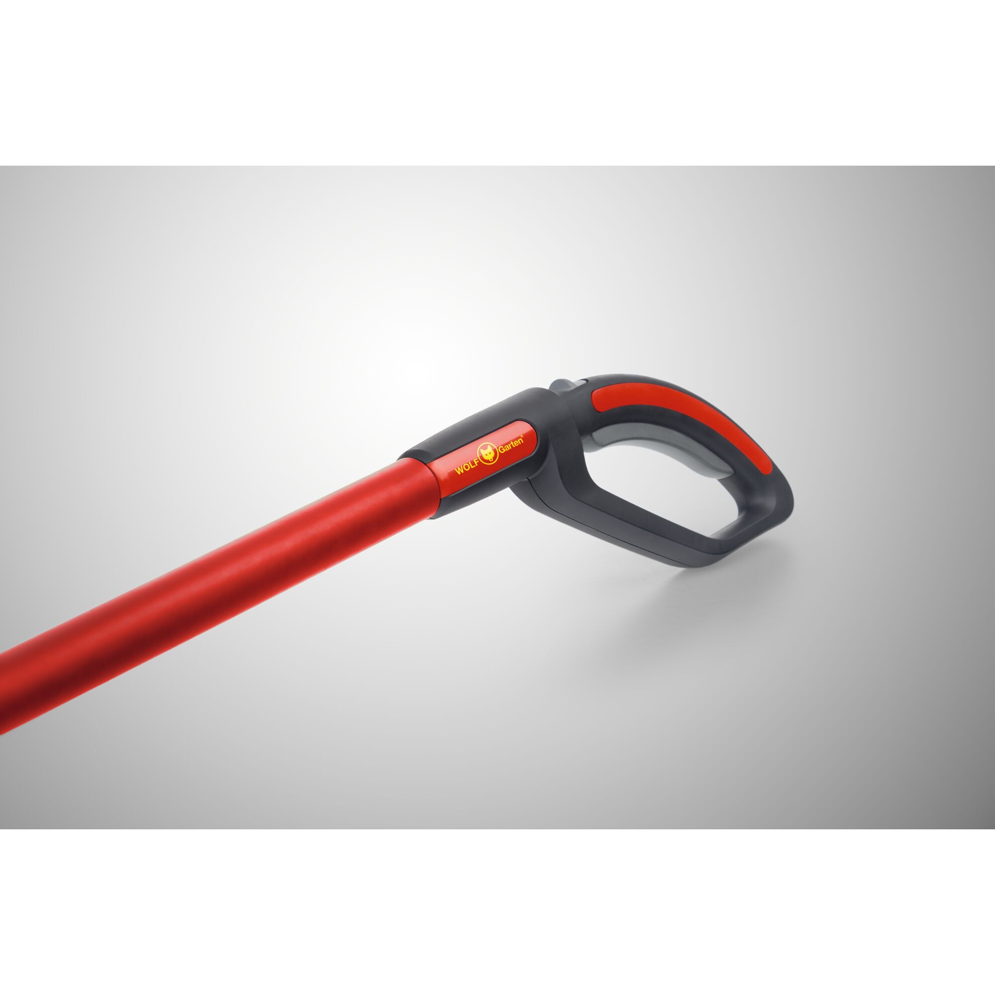 Close-up of a red and black WOLF Garten handle with ergonomic grip, featuring a yellow brand logo and a gray background.