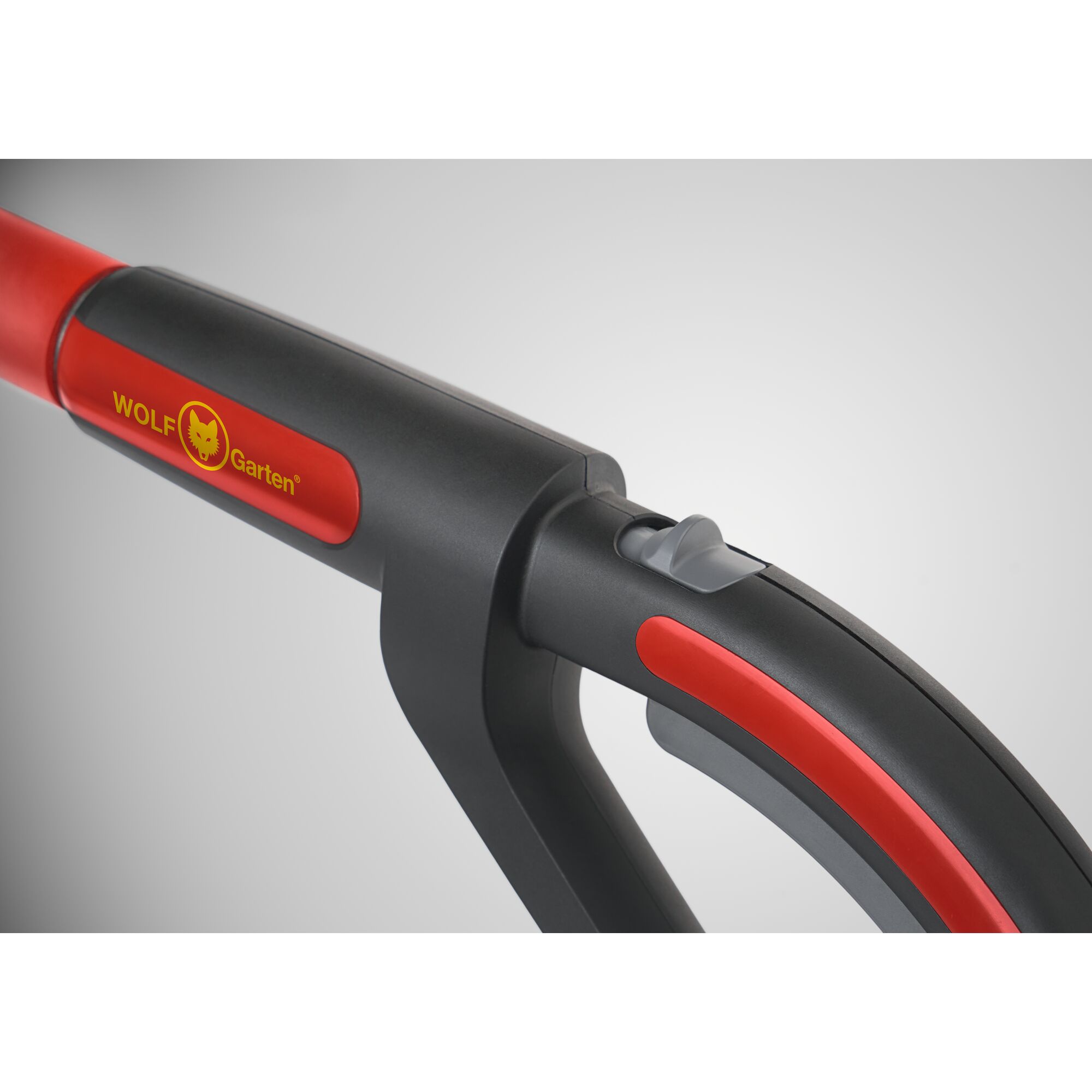 Close-up of a handle with a grey and red design, featuring the WOLF-Garten logo and branding on the side. The handle includes a grey button or lever.