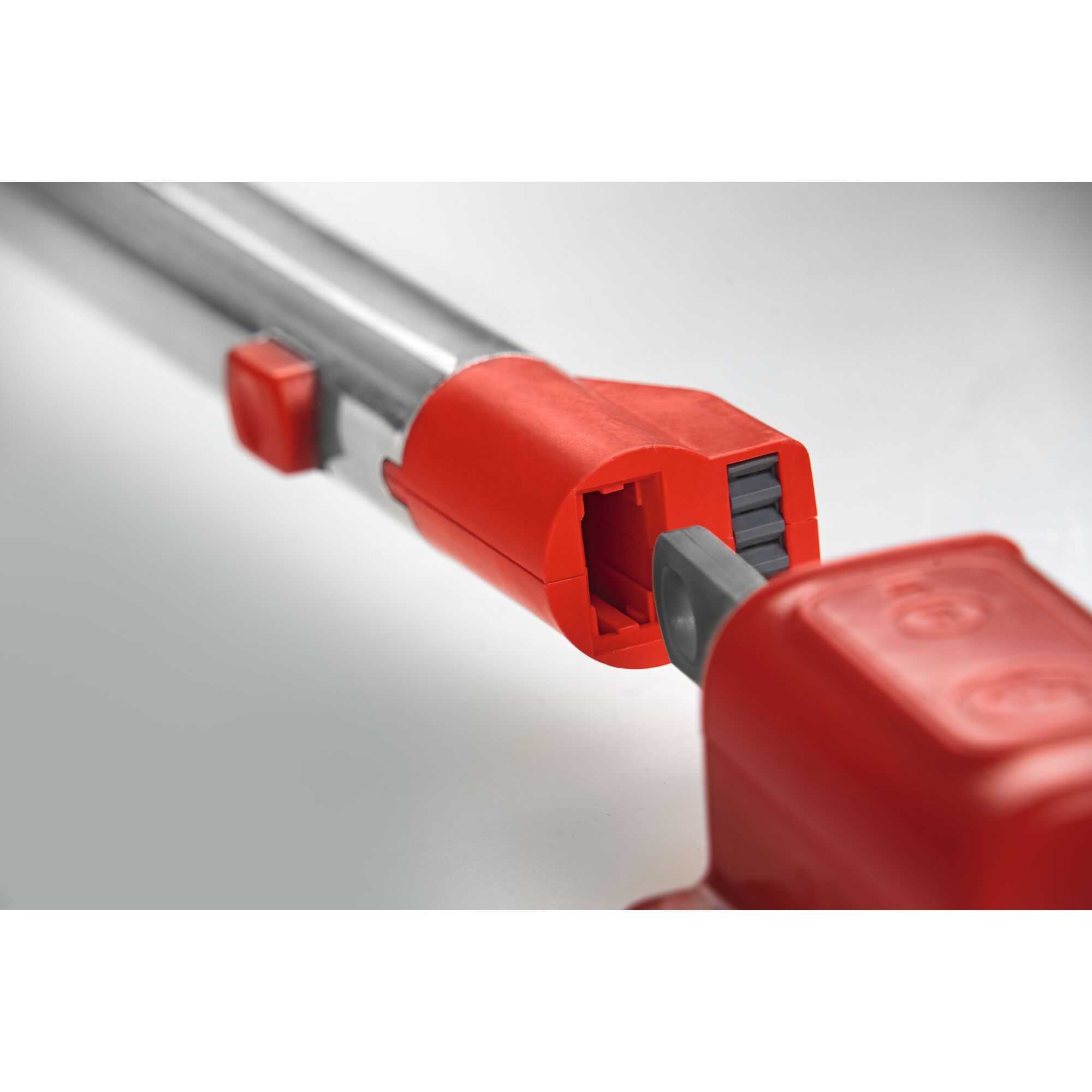 Close-up image of a metal gardening tool handle with a red plastic connector for attaching accessories, showing the connection mechanism.