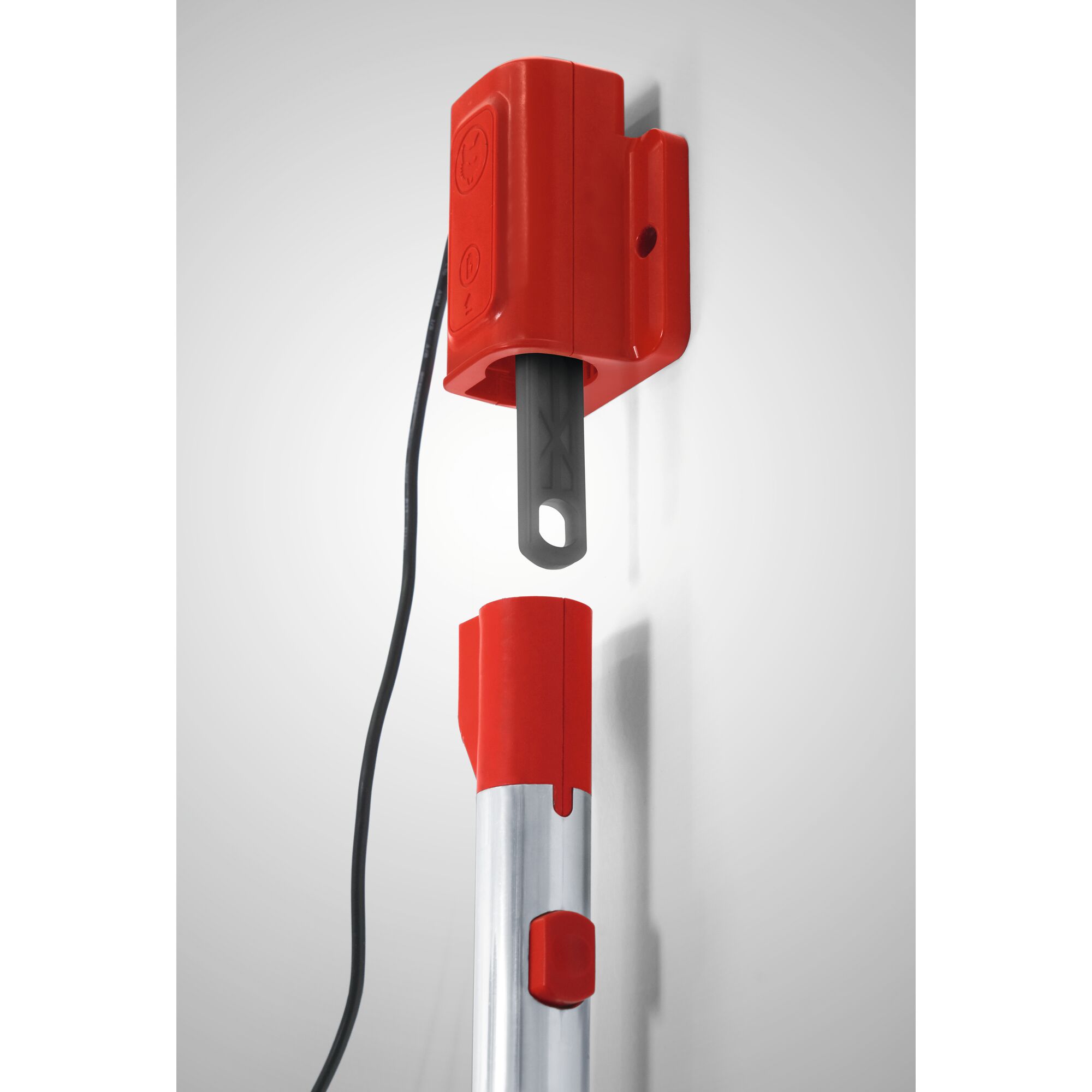 A close-up image of a wall-mounted red and silver garden tool holder, featuring a red plastic bracket with an attached cord and a metal tool handle positioned below for storage.