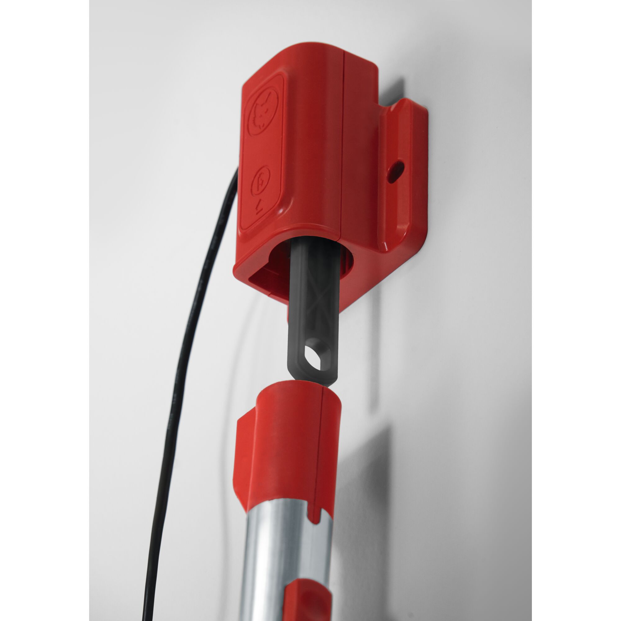 Close-up of a red wall-mounted tool holder with a metal handle inserted, designed for organizing and storing garden tools.