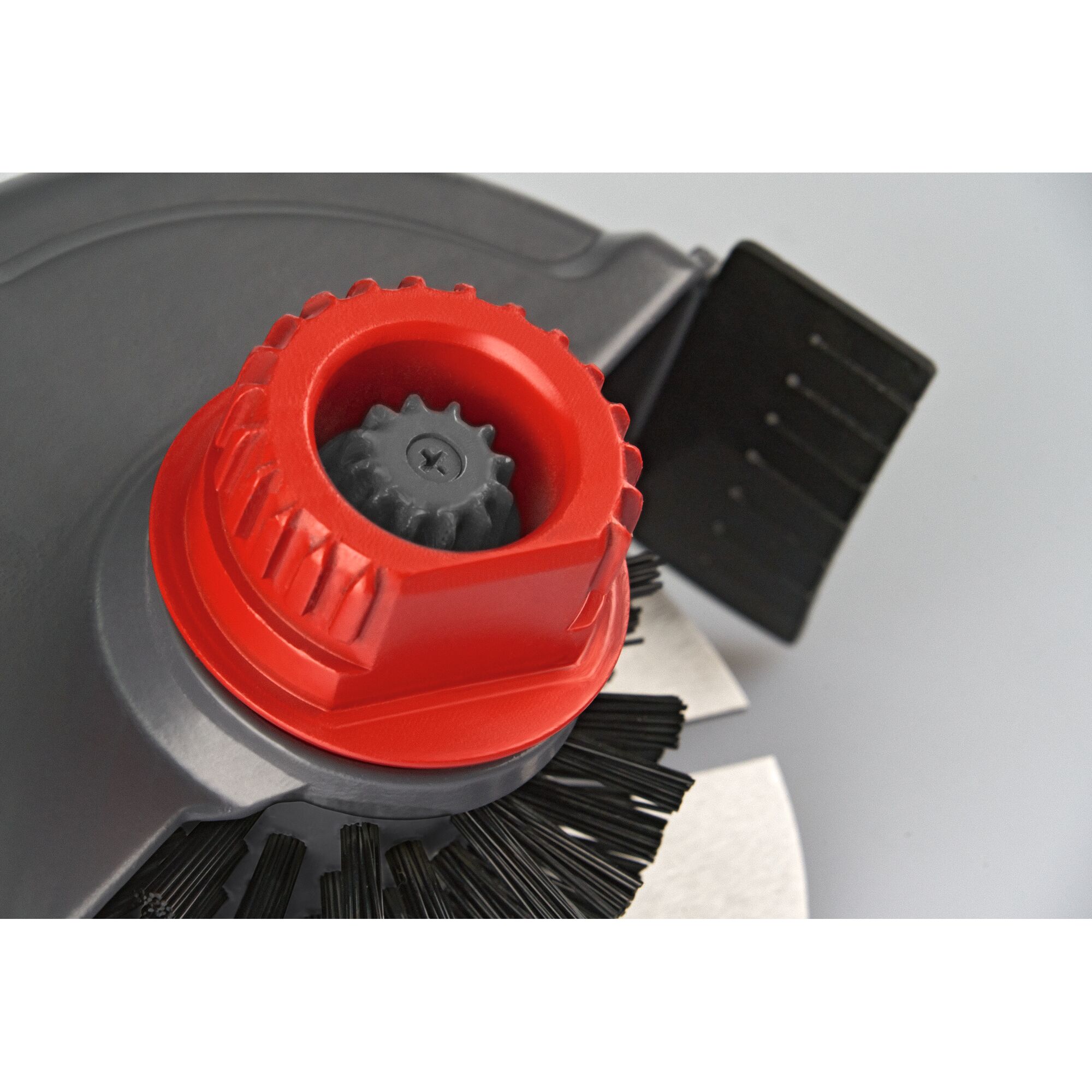 Close-up view of a mechanical component with a red gear and black bristles, likely part of a garden cleaning tool.