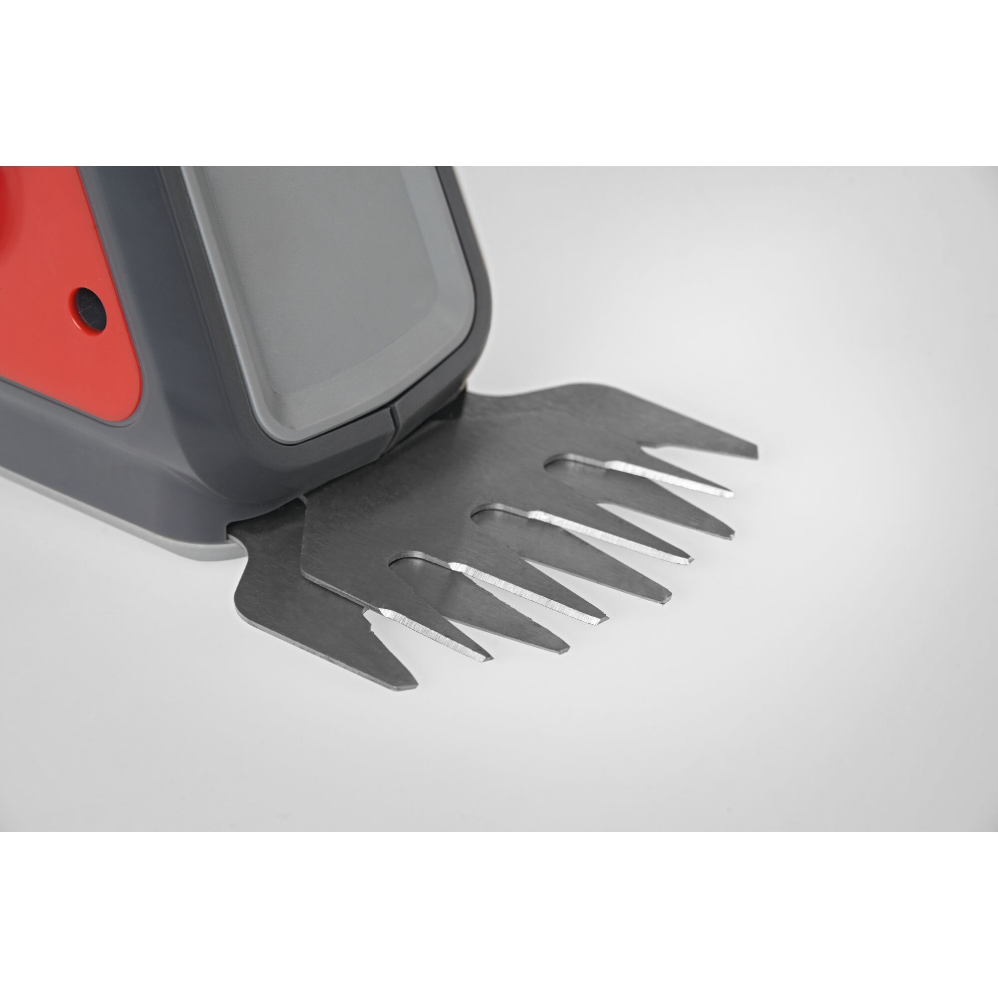 Close-up view of the blade attachment on a WOLFGarten electric grass shear, showing the silver metal cutting blades and red and grey plastic housing.