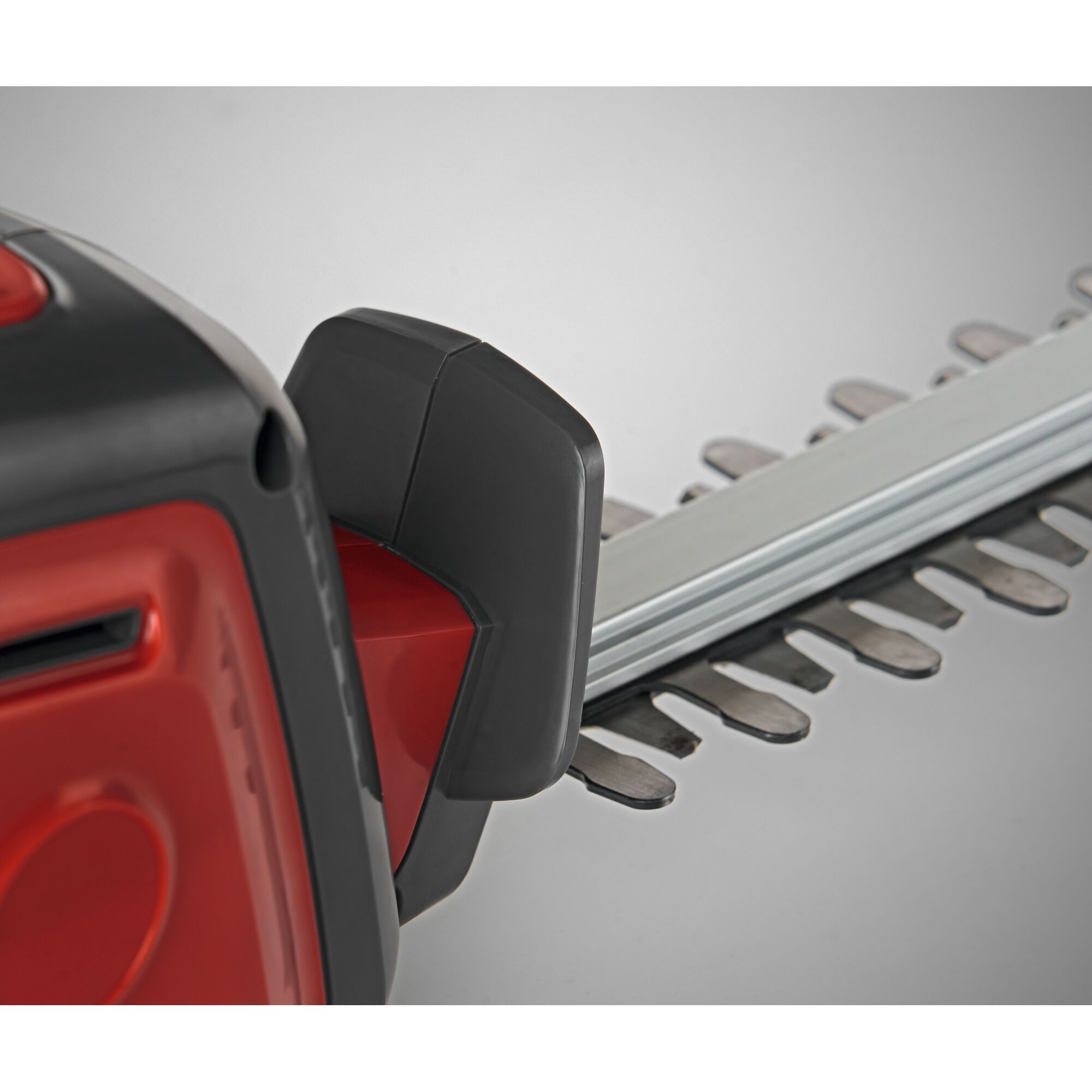 Close-up view of a red and black electric hedge trimmer showing the handle and part of the cutting blades.