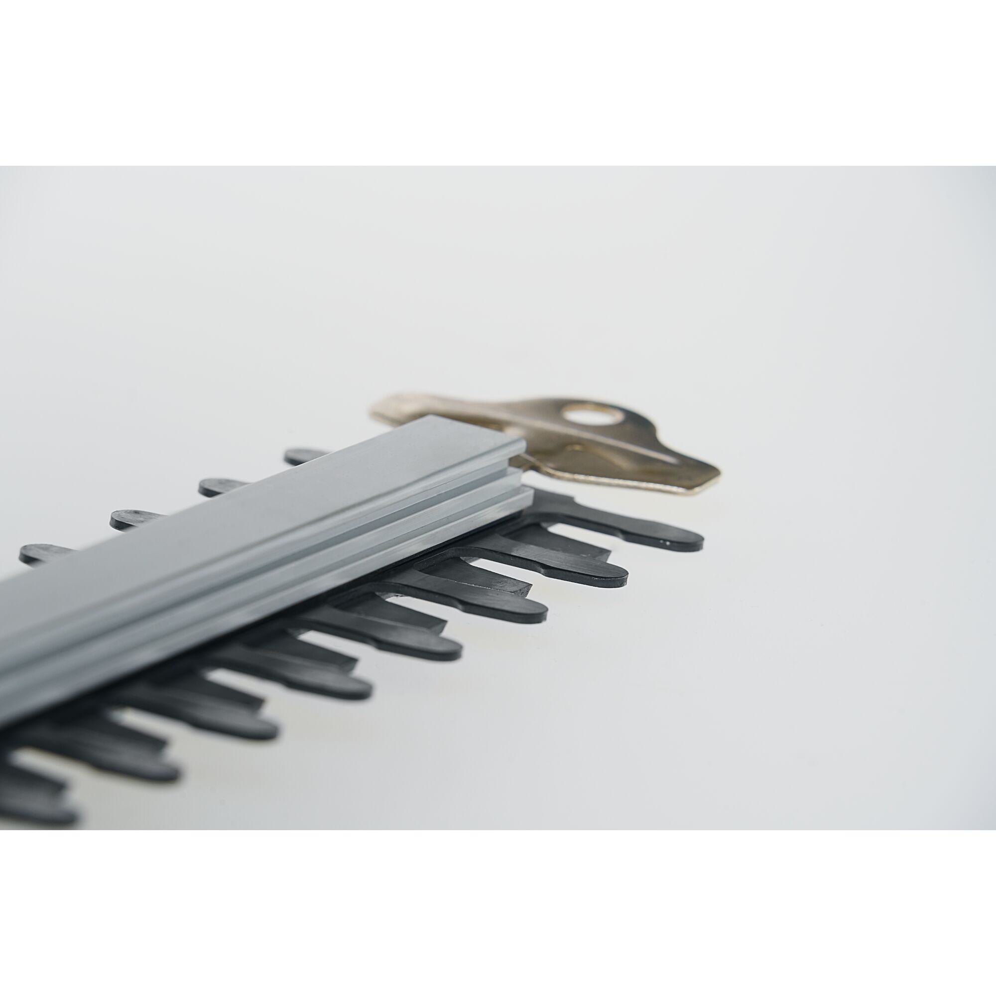 Close-up view of the blade section of a hedge trimmer with sharp metal teeth and a metallic attachment piece, placed on a white surface.