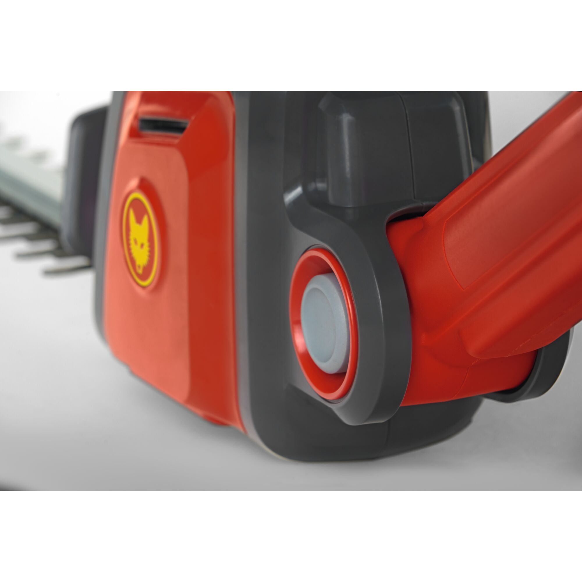 Close-up of a WOLFGarten garden tool, featuring a red and grey body with a yellow wolf head logo. The image shows a detailed view of the tool's joint and blade section.