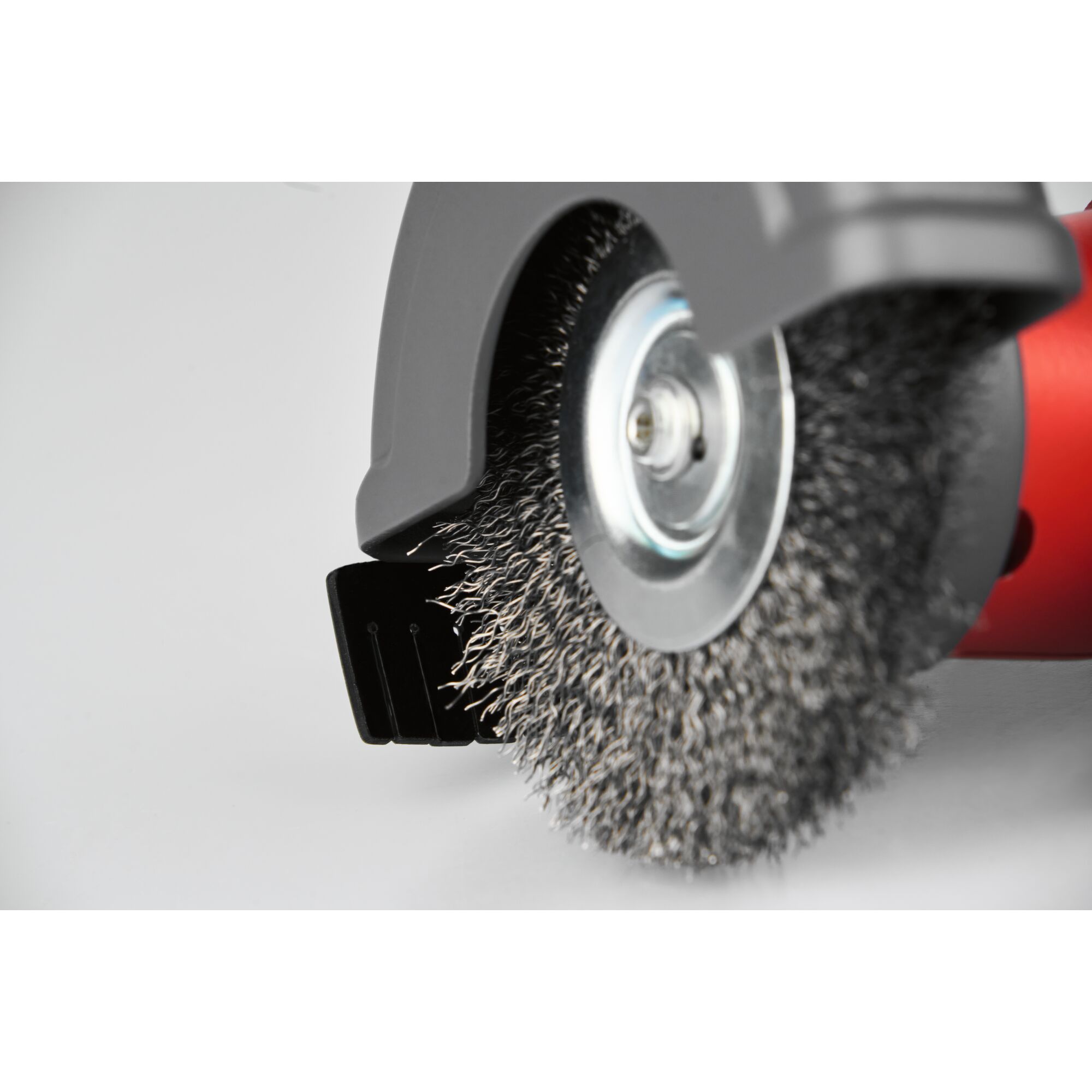 Close-up of a wire brush wheel attached to a red power tool, partially covered by a safety guard.