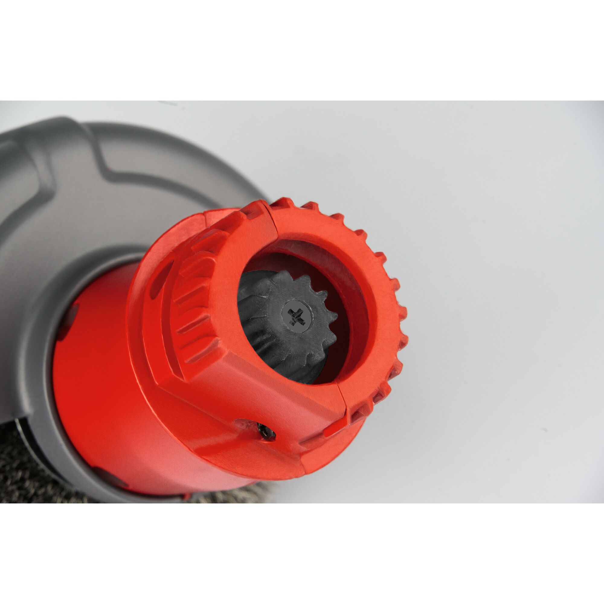 Close-up view of a red mechanical tool part with a black gear component, likely part of a garden tool attachment. The background is plain and light-colored.