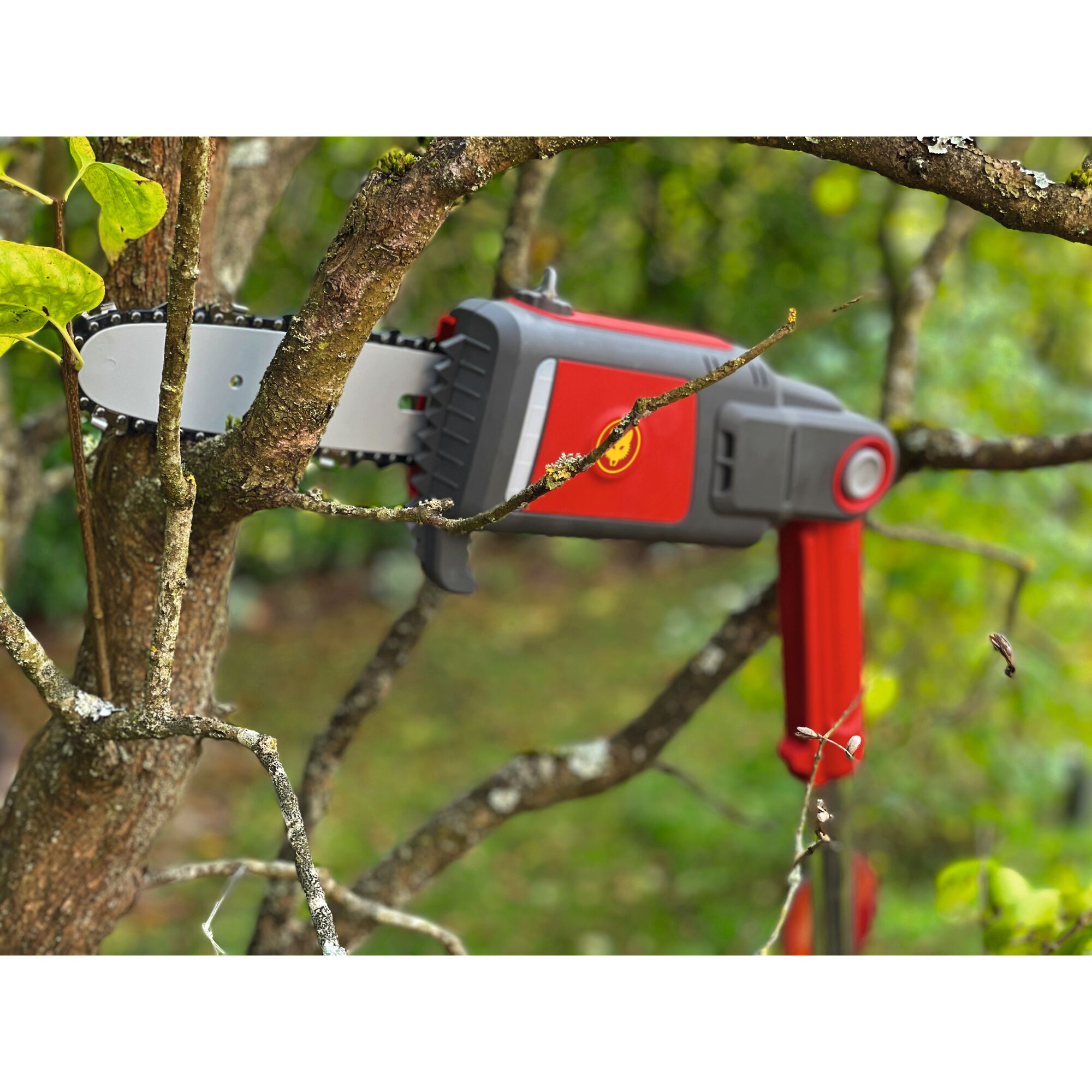 A red and grey electric pruning saw from WOLFGarten is cutting a tree branch outdoors.
