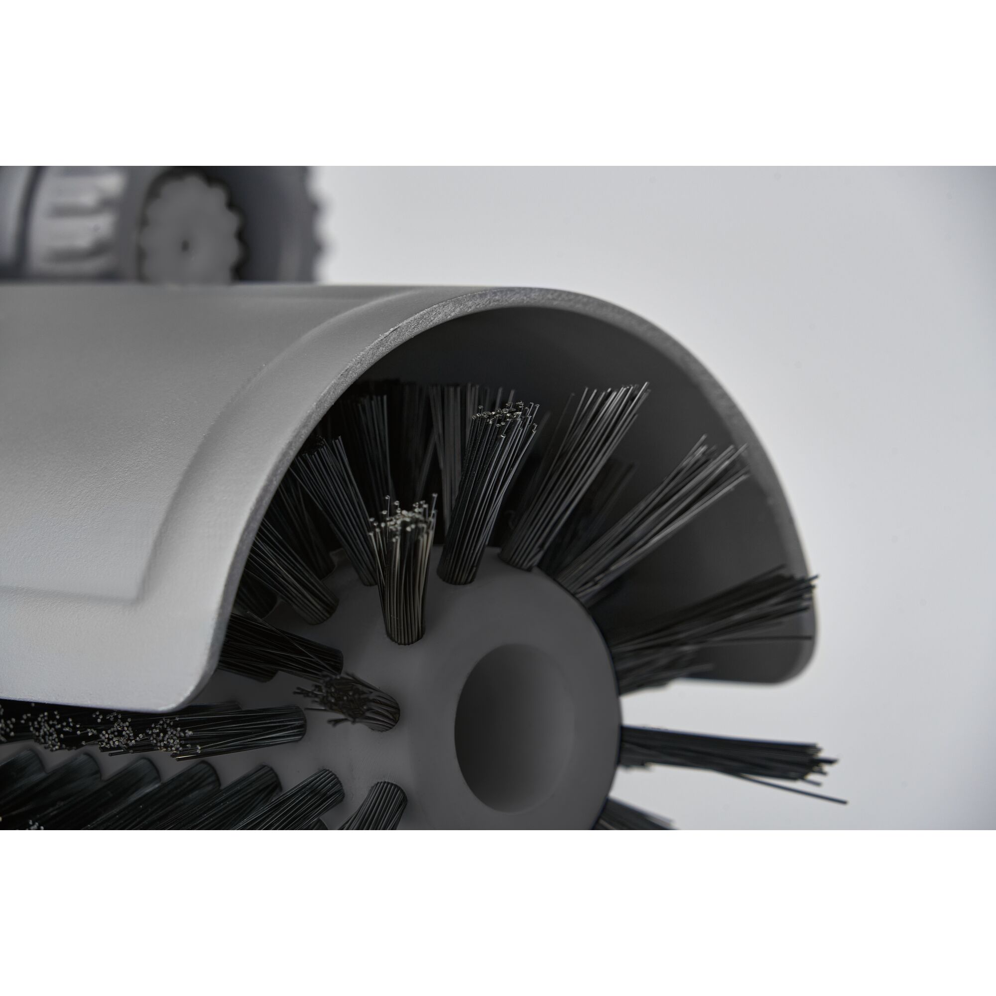 Close-up image of a cylindrical brush with stiff bristles, partially covered by a protective gray casing. The brush is part of a mechanical cleaning device.