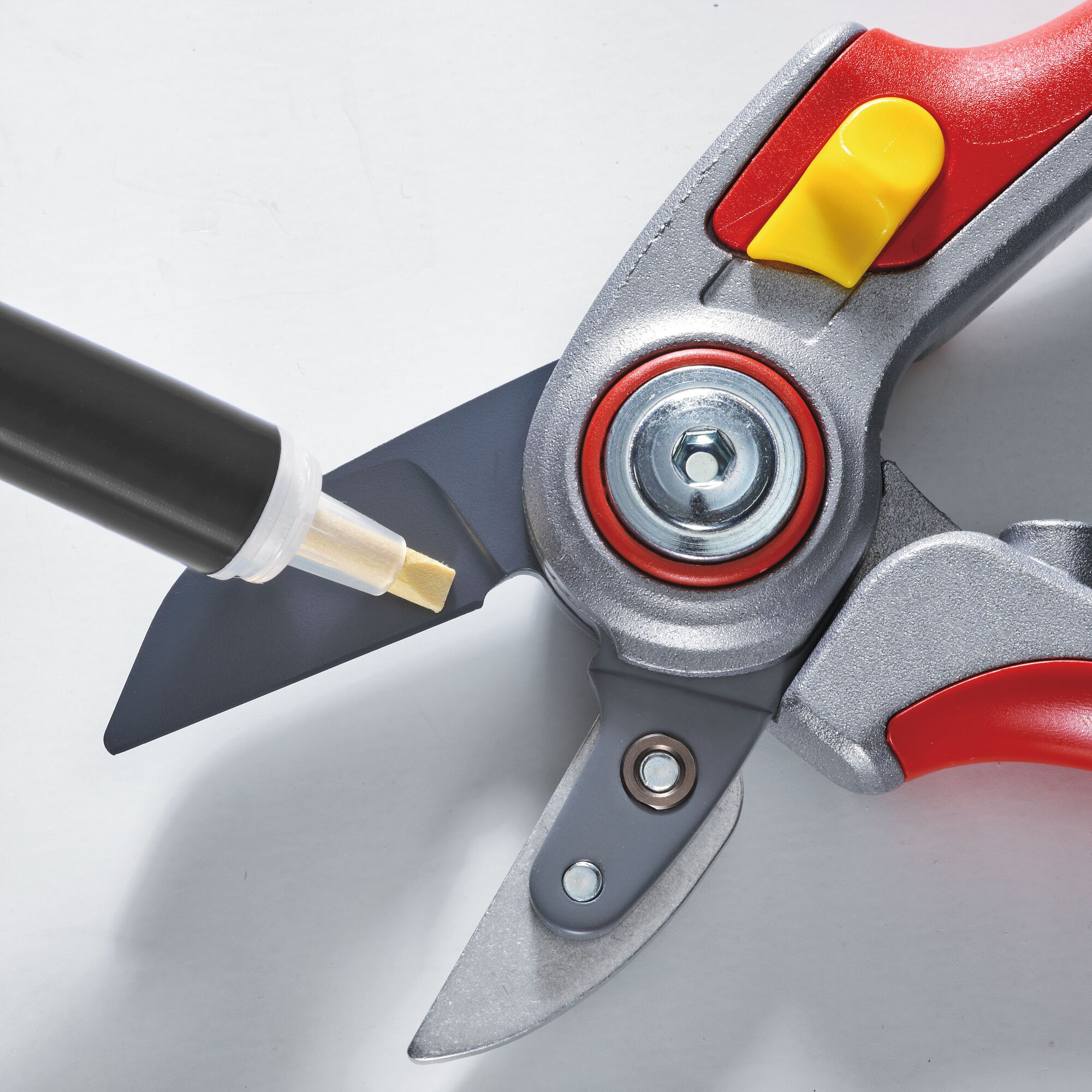 Close-up of a garden pruning shear with a red and yellow handle being sharpened with a tool.