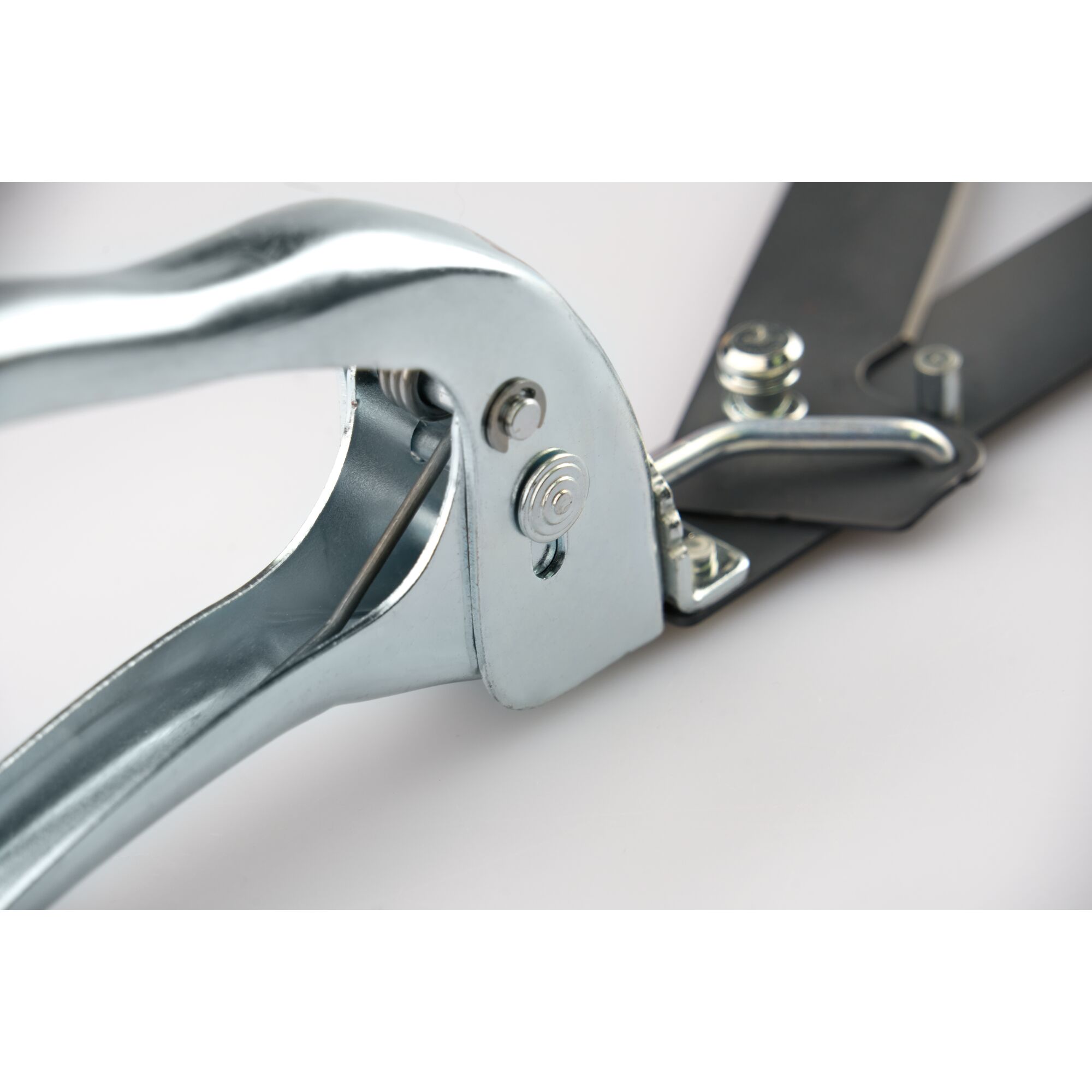 Close-up view of a metal garden tool with a spring mechanism, likely a pair of hedge shears or pruning scissors, showing the handle and hinge details.