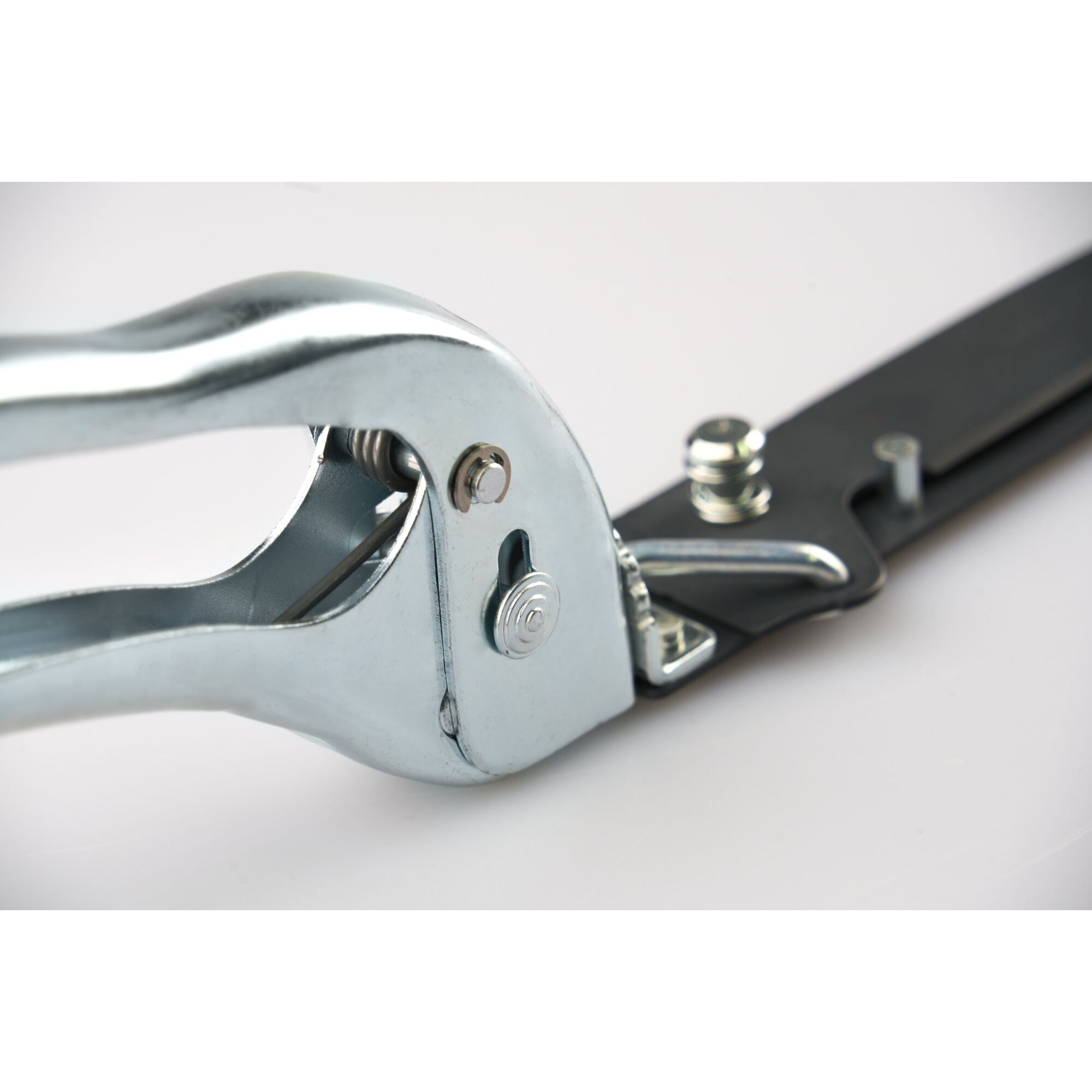 Close-up of a metal ratchet mechanism on a garden tool, featuring shiny handle and bolts attached to a black blade.