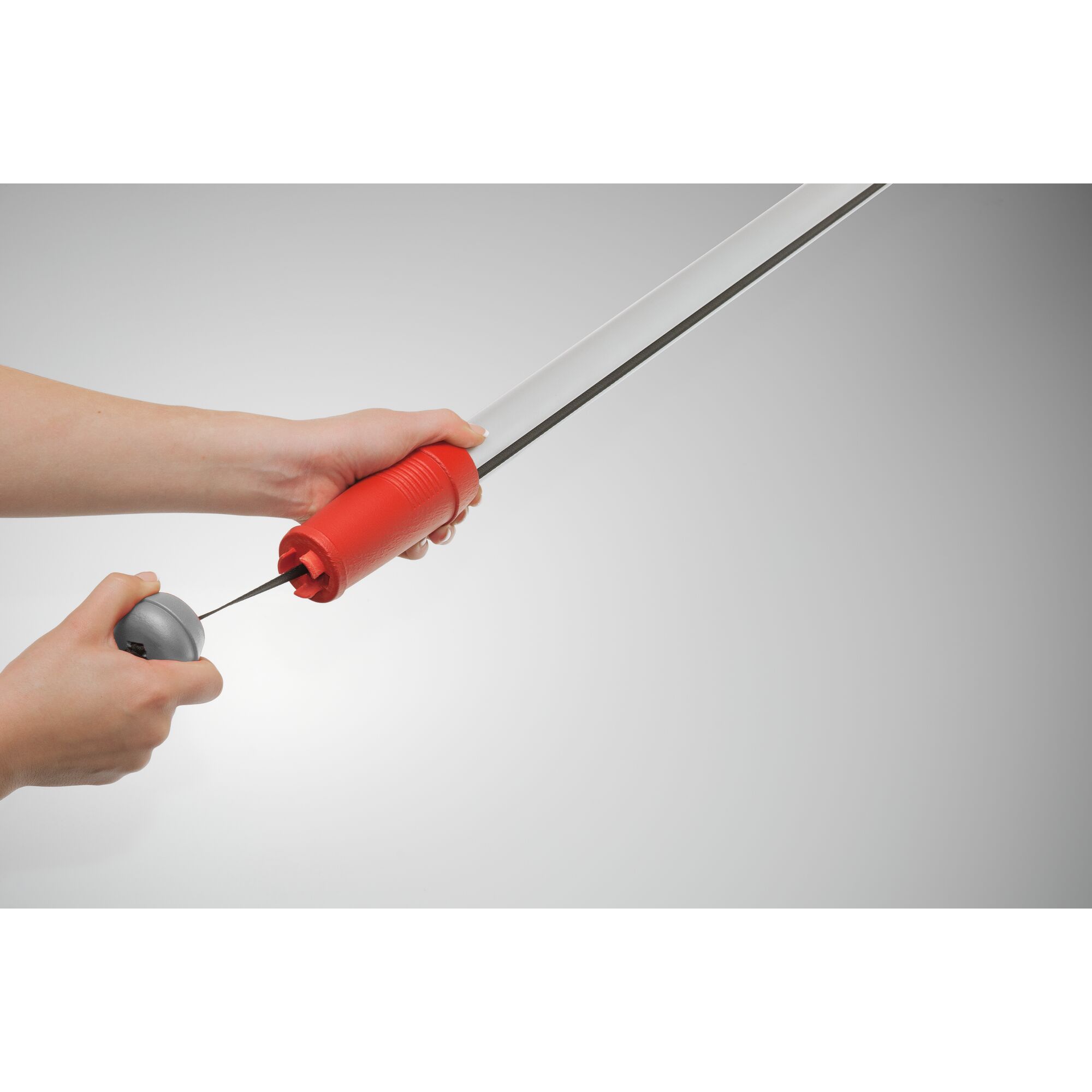 Close-up of hands attaching a red and silver garden tool, likely a handle to a pole or extension for a WOLFGarten product, against a neutral background.