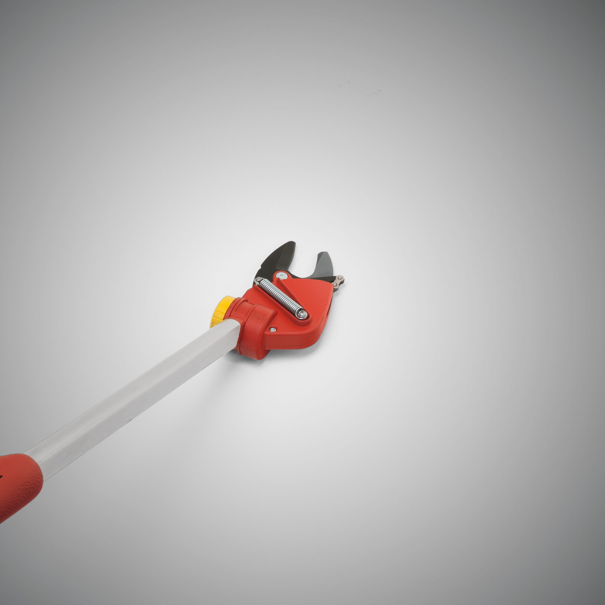A close-up of a garden pruner with a red and yellow handle, featuring a metal cutting blade and spring mechanism, photographed on a plain light background.