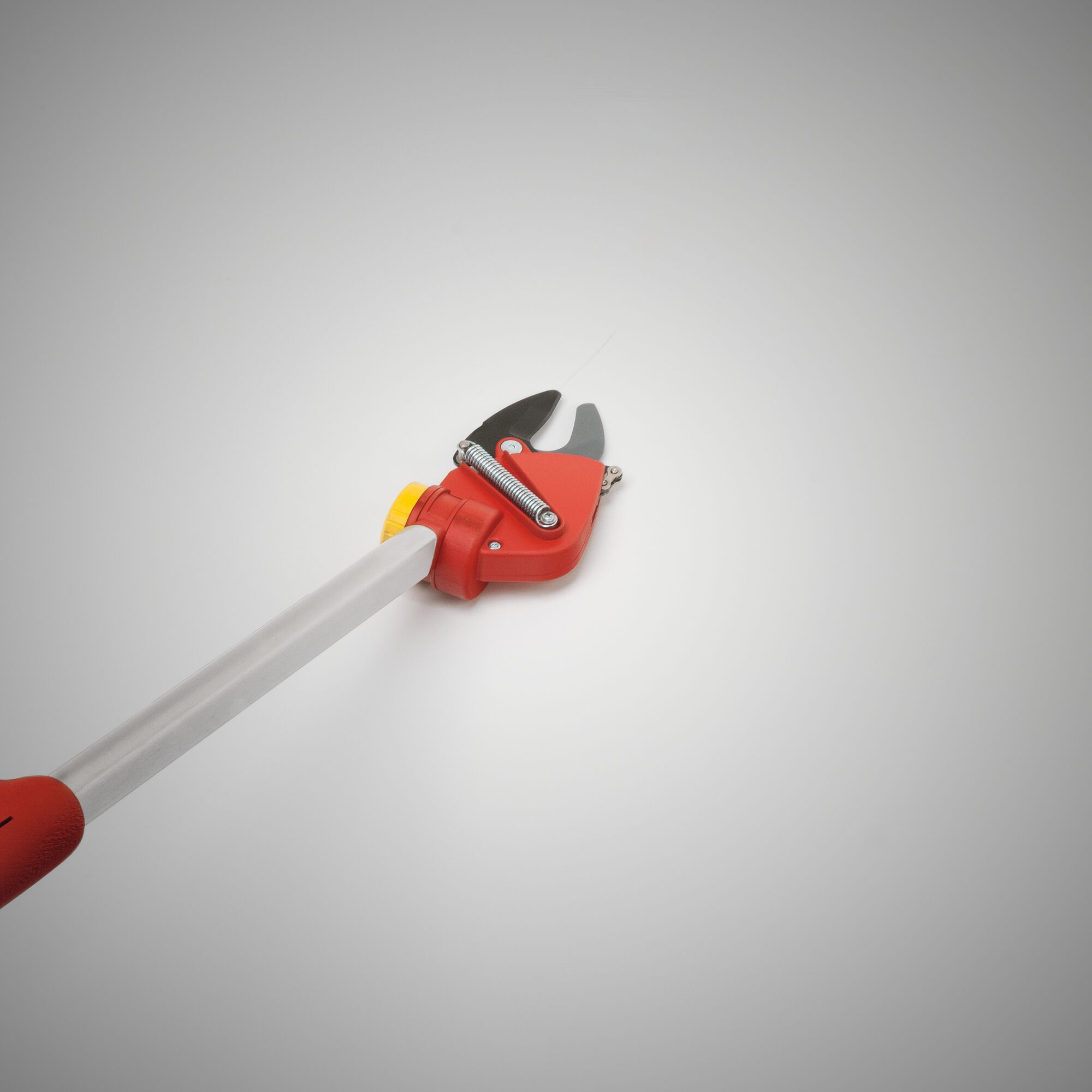 A close-up image of a WOLF-Garten telescopic bypass lopper with a red and yellow handle and metal cutting blades, used for trimming branches and gardening tasks.