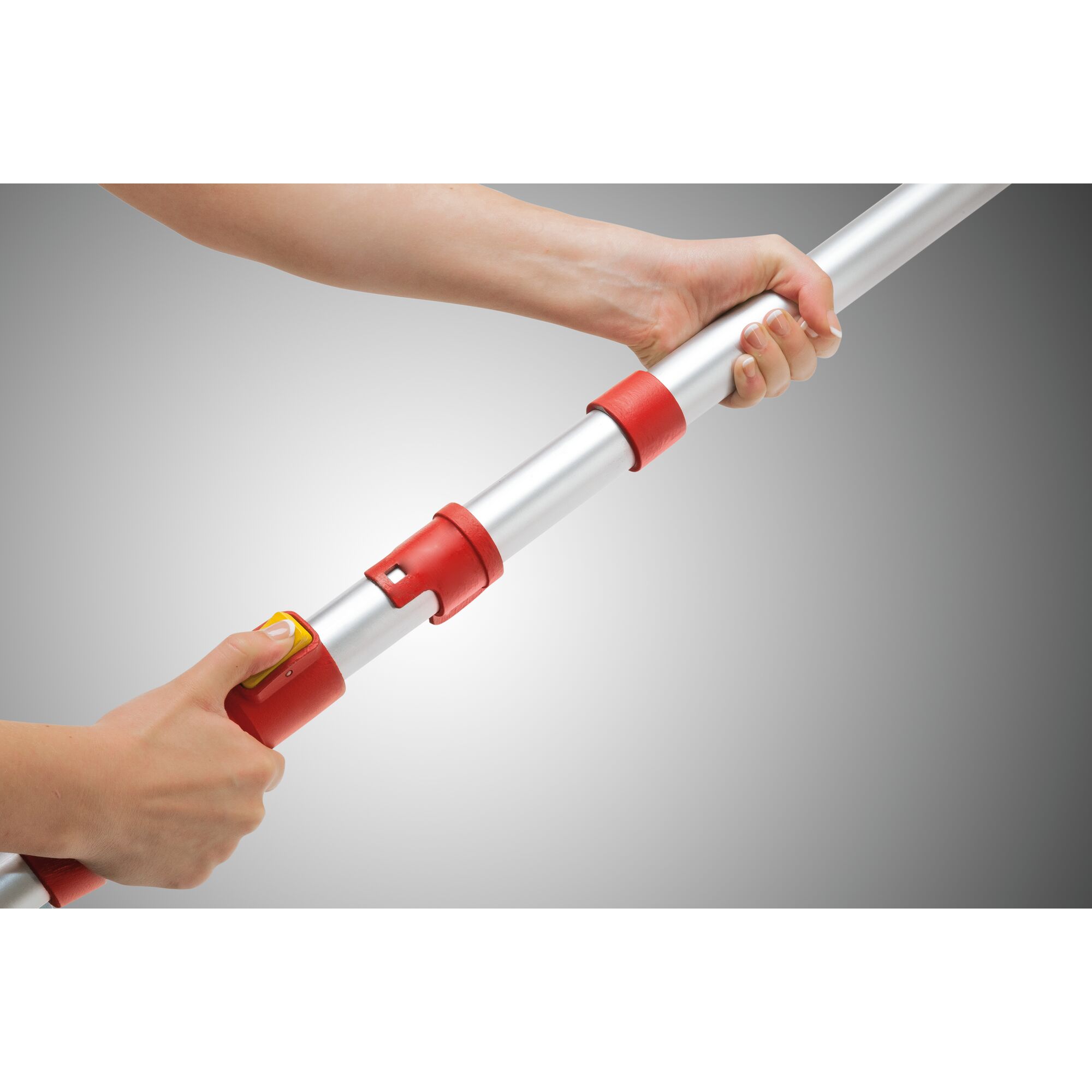 Close-up of two hands adjusting a telescopic aluminum pole with red connectors and a yellow button, demonstrated against a neutral gray background.