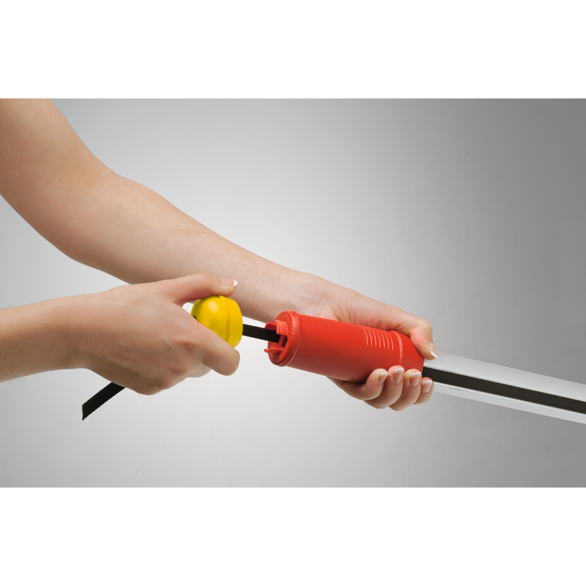 Close-up of hands attaching a yellow component to a red handle tool, with a black strip and metal blade. The tool is likely used for gardening or maintenance.
