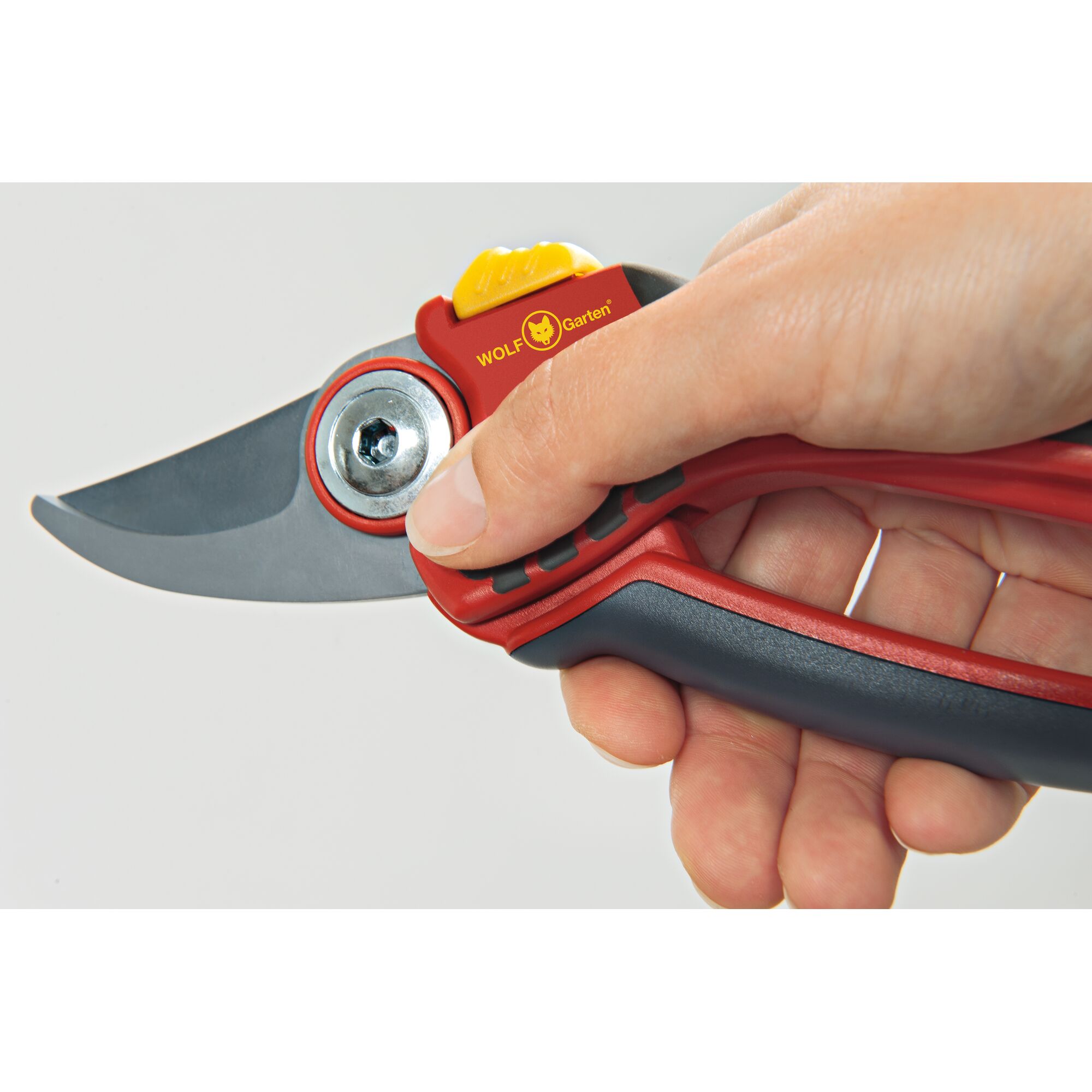 A close-up view of a hand holding a red and black WOLF Garten gardening pruner with a metal blade.