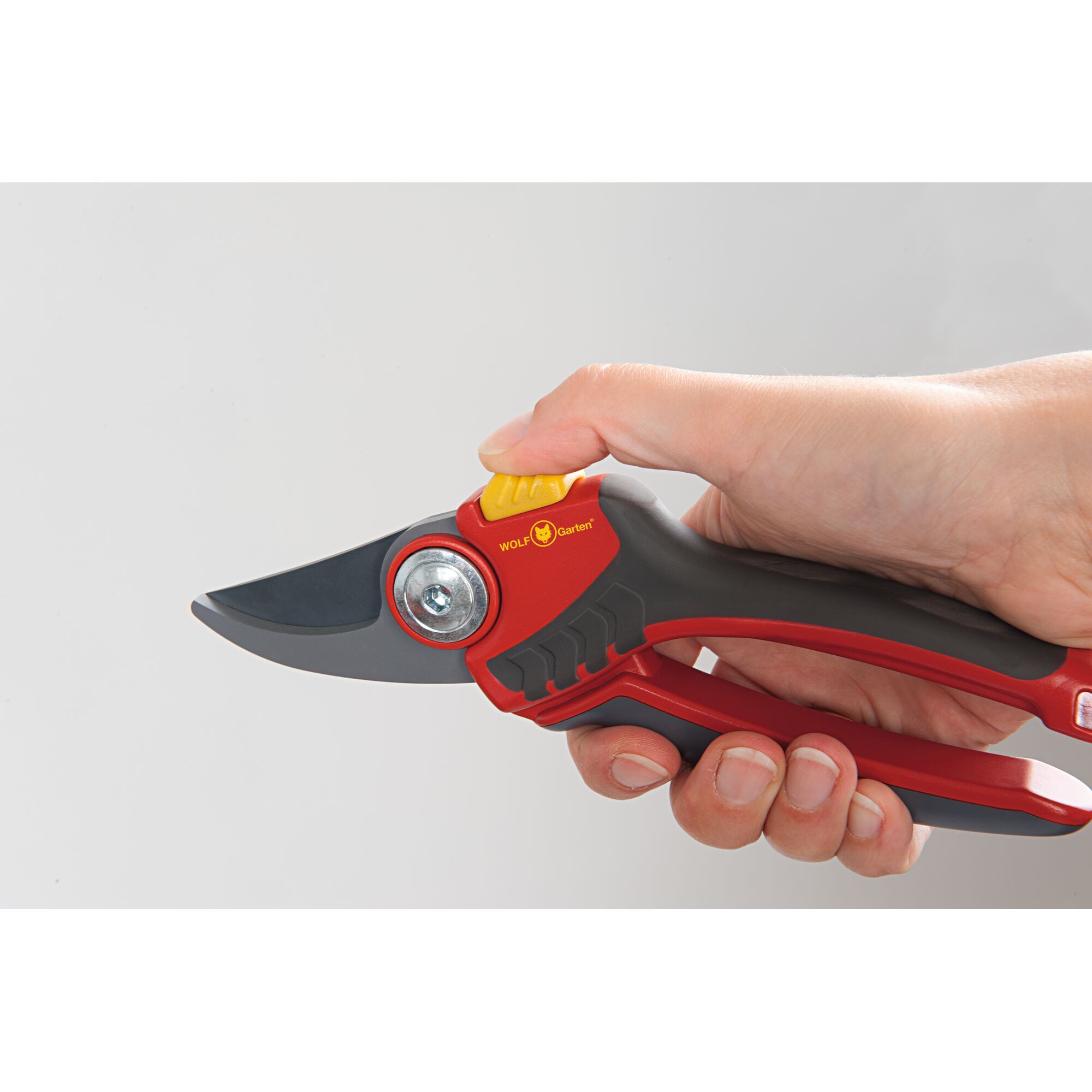 A close-up of a hand holding a red and black WOLF Garten pruning shear, designed for gardening tasks.