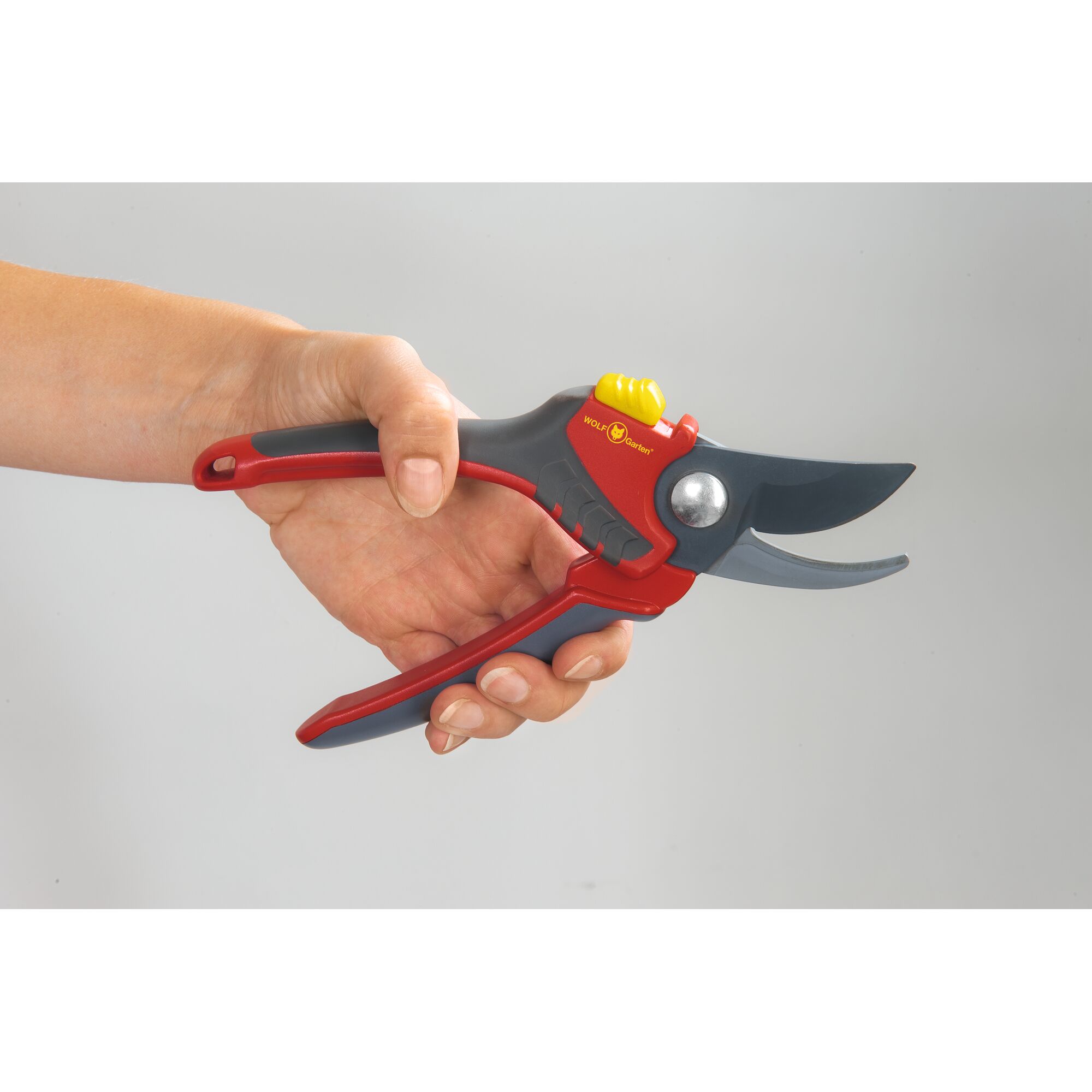 A hand holding a WOLFGarten garden pruning shear with red, grey, and yellow accents, suitable for cutting plants.