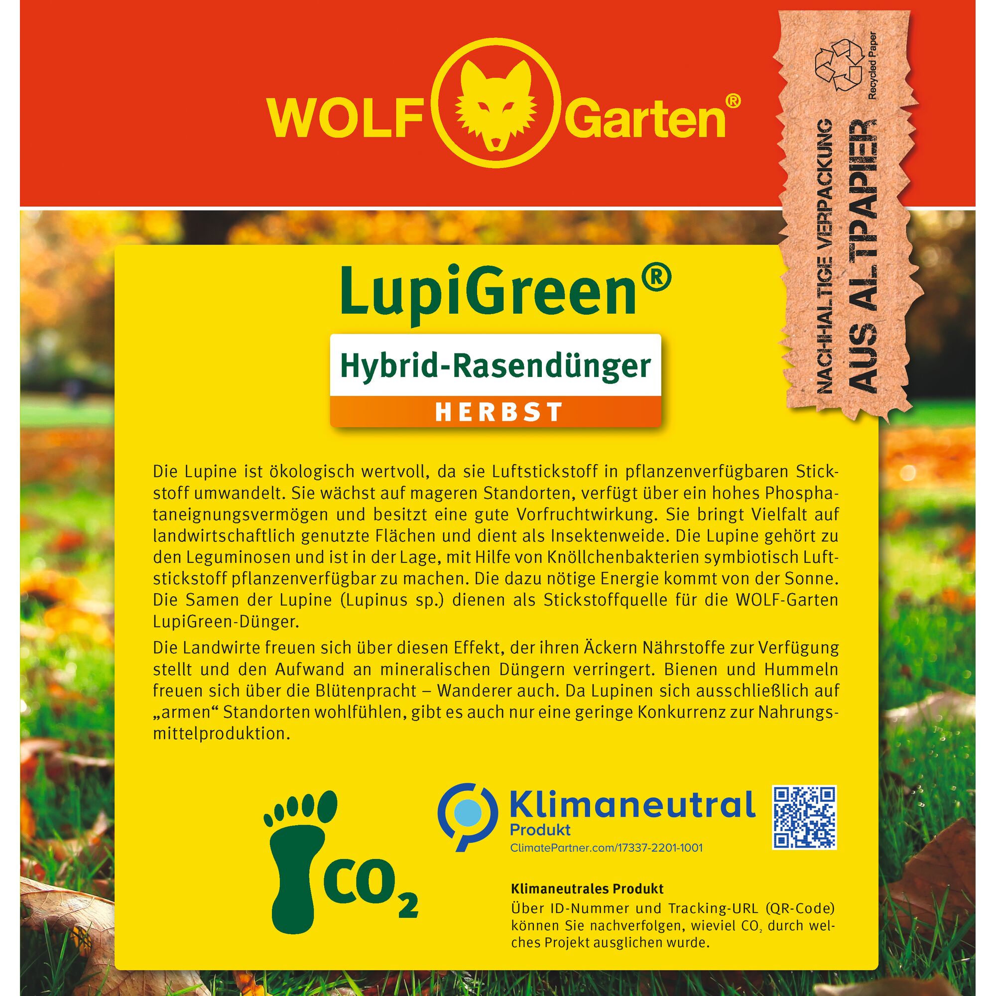 Front packaging of WOLF Garten LupiGreen Hybrid Lawn Fertilizer (Autumn), mostly yellow with information about ecological value of lupine, fertilizer features and climate-neutral product claims. Includes a brown label stating sustainable packaging made from recycled paper. The bottom section has CO2 footprint and KlimaNeutral branding. Background shows a blurred lawn and trees.